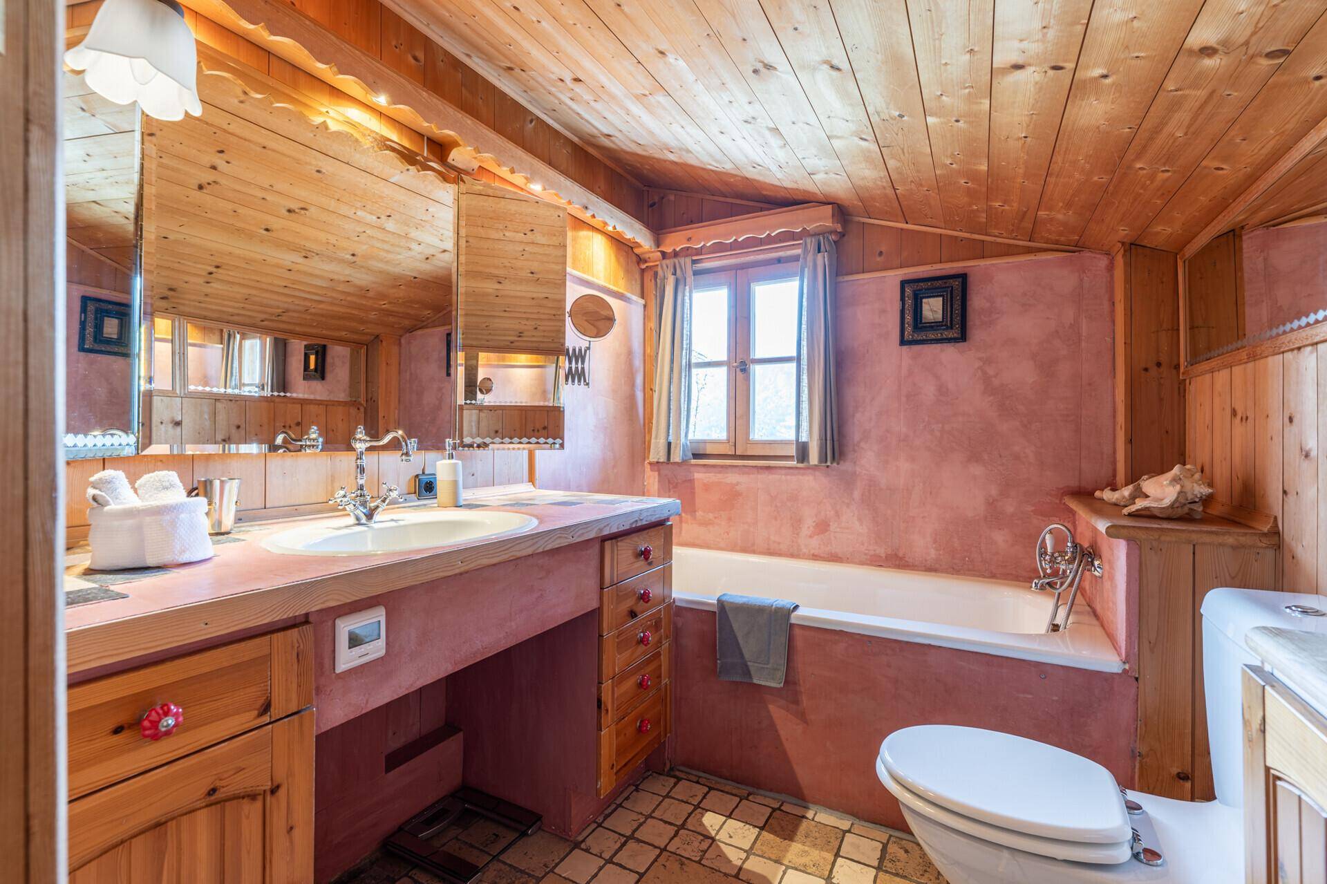 Gemütliches Badezimmer mit Badewanne, Holzverkleidung und Fenster für natürliches Licht.