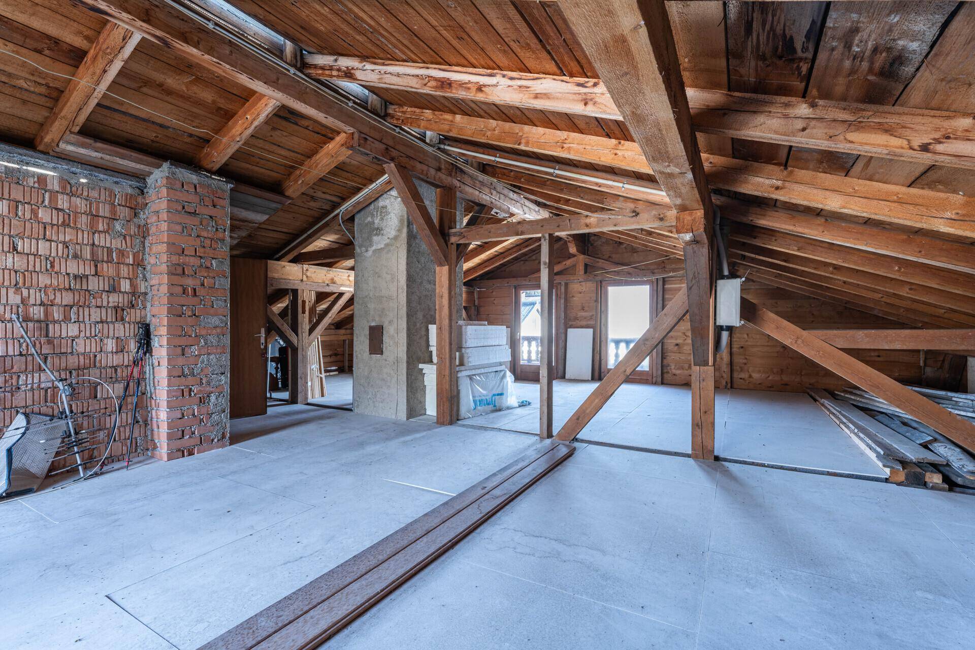 Unausgebauter Dachboden mit sichtbaren Holzbalken und Ziegelwänden, ideal für einen Ausbau.