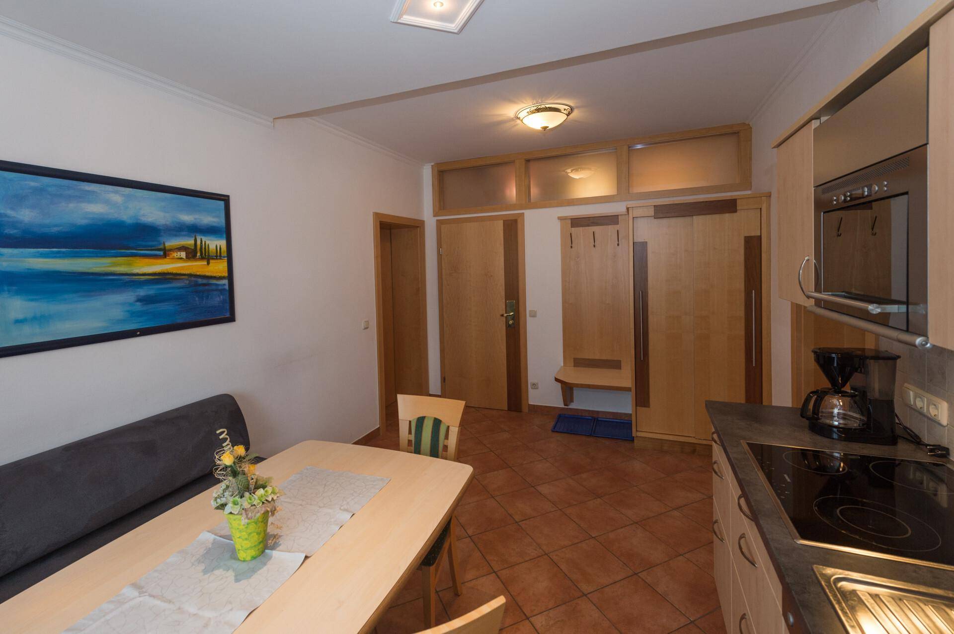 Funktionale Küchenzeile mit Essbereich und integrierten Geräten, ergänzt durch einen Eingangsbereich mit Garderobe.