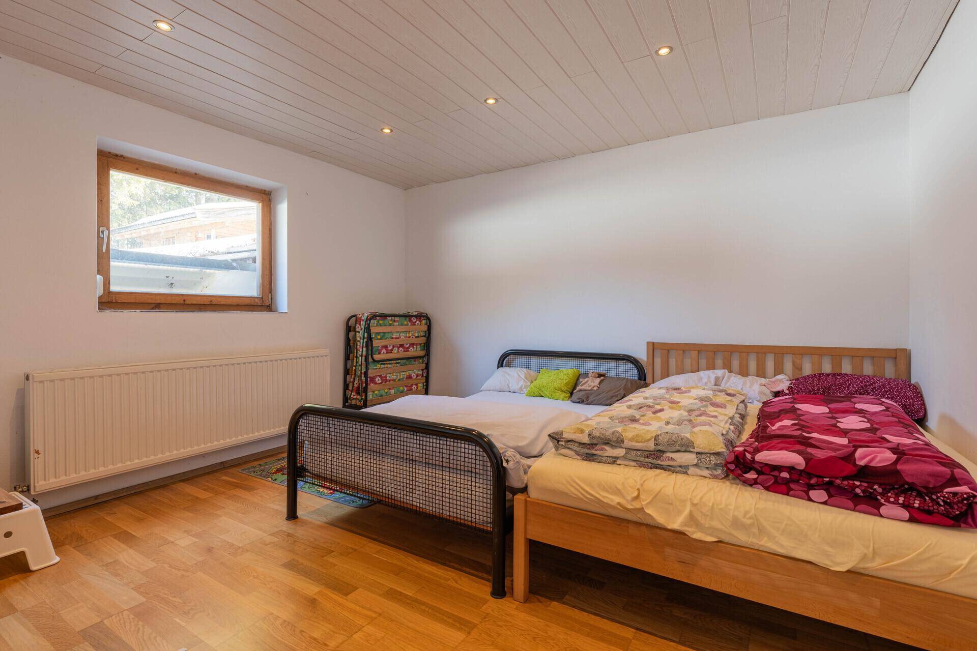 Schlafzimmer mit Holzboden, zwei Betten und einer Holzdecke mit Einbaustrahlern.