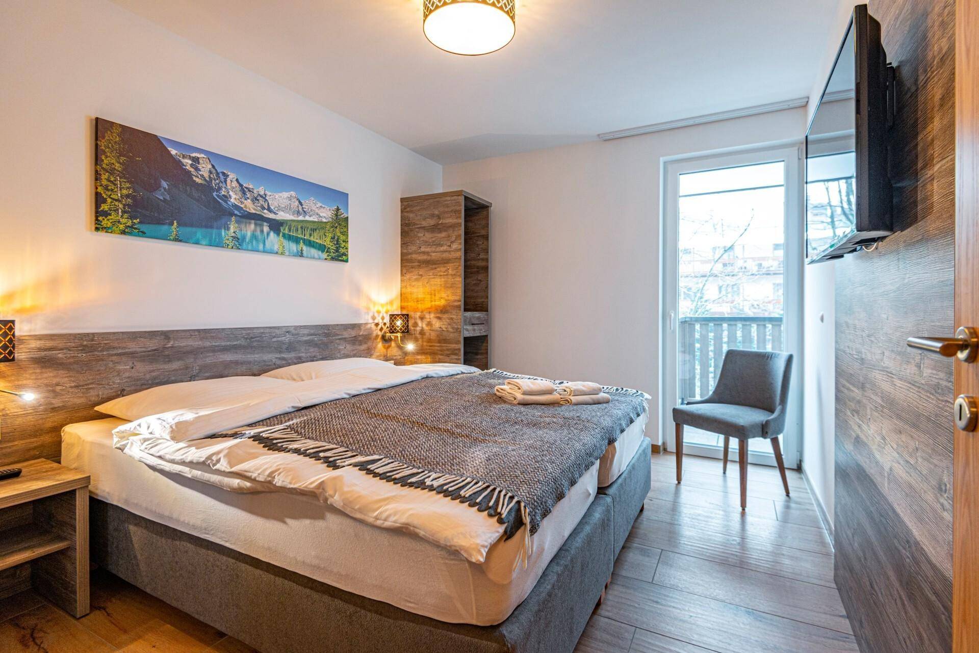 Komfortables Schlafzimmer mit Doppelbett, Holzboden und Zugang zu einem kleinen Balkon.