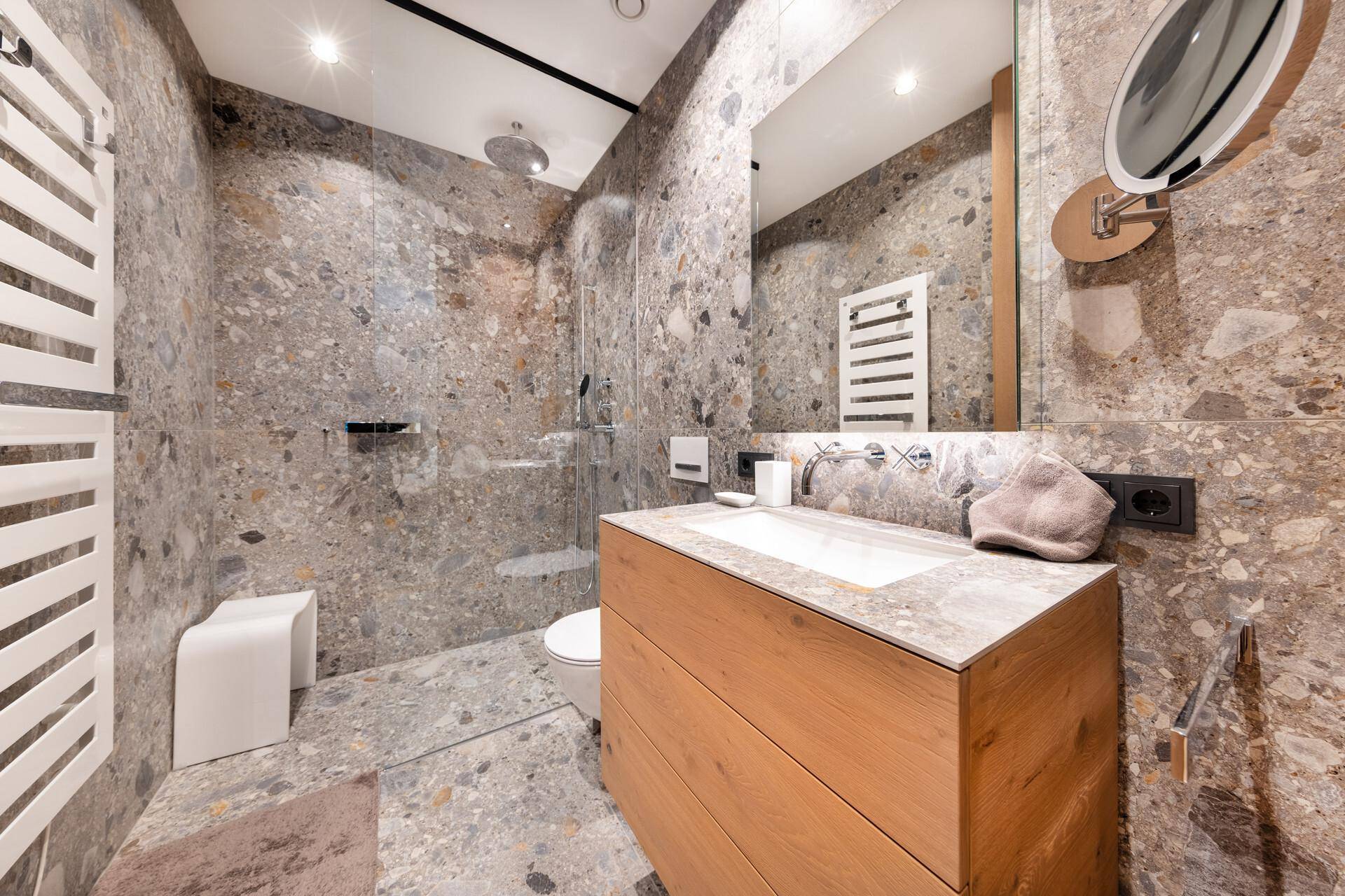 Stilvolles Badezimmer mit Steinfliesen, moderner Dusche und Waschtisch mit Spiegel.