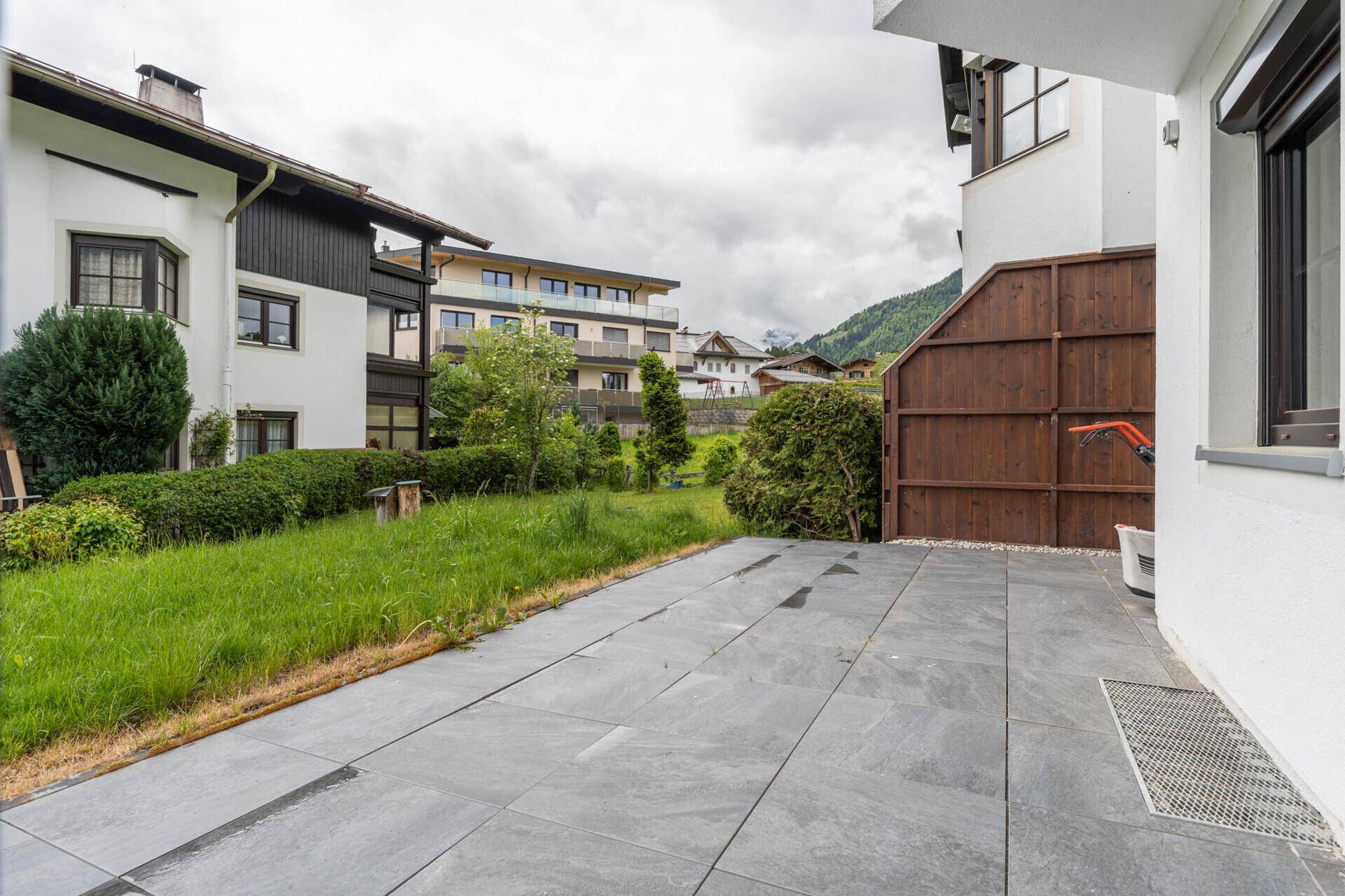 Große gepflasterte Terrasse neben einem Rasenbereich mit Blick auf die umliegenden Häuser.