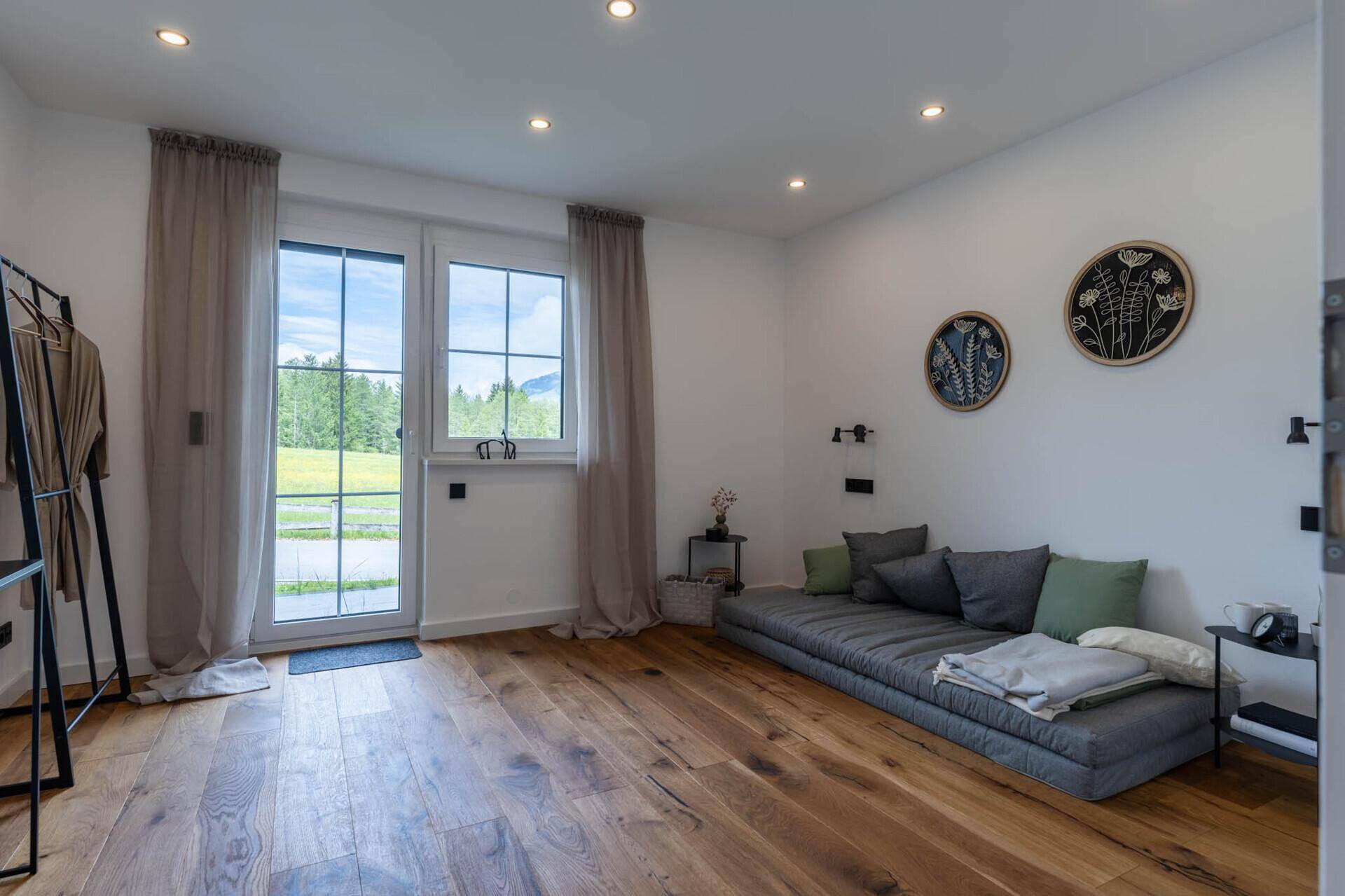 Schlafzimmer mit Holzboden, großem Fenster und direktem Blick auf die grüne Landschaft und Berge.