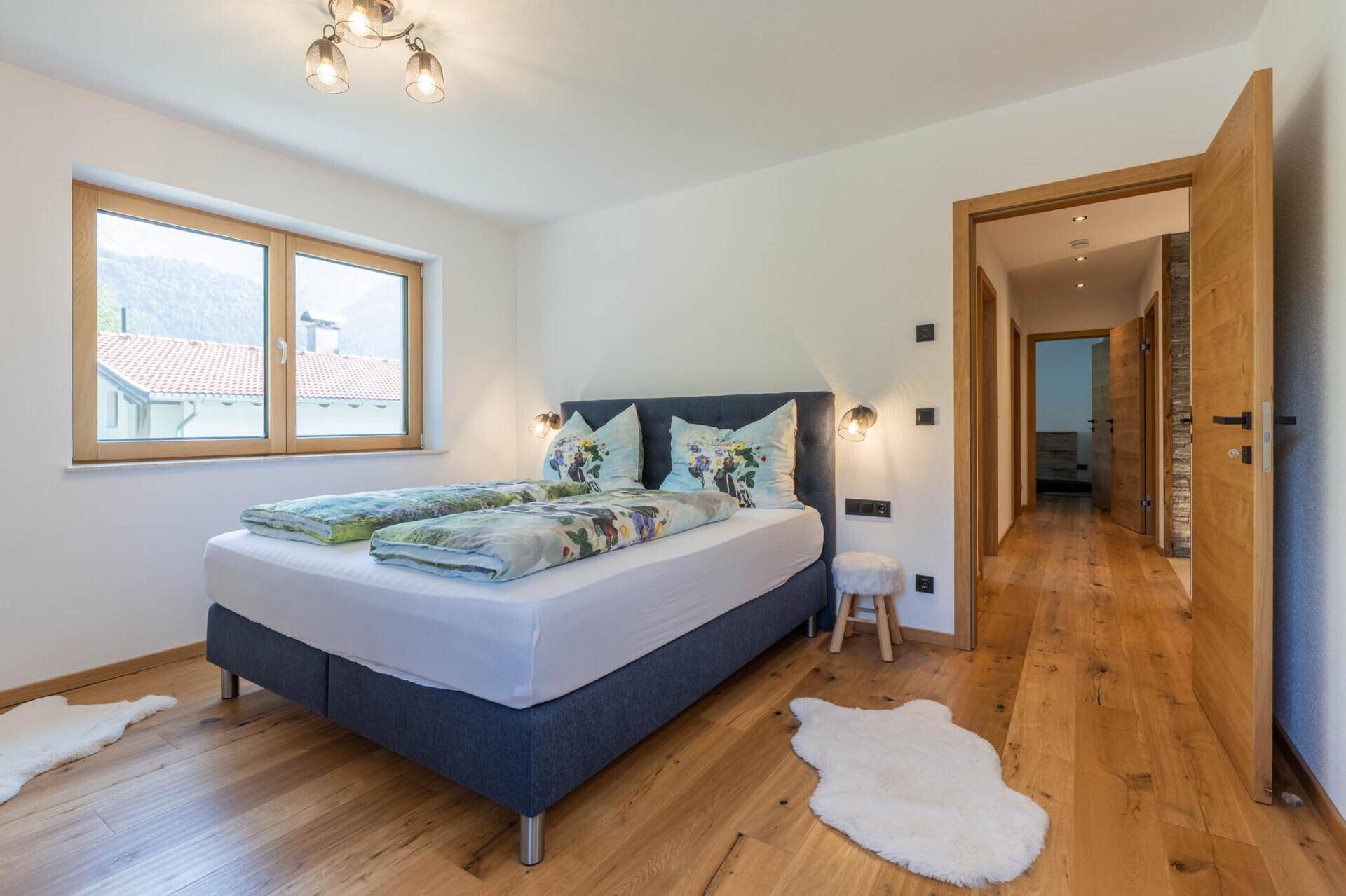 Helles Schlafzimmer mit Holzboden, Doppelbett und Blick auf die umliegende Berglandschaft.