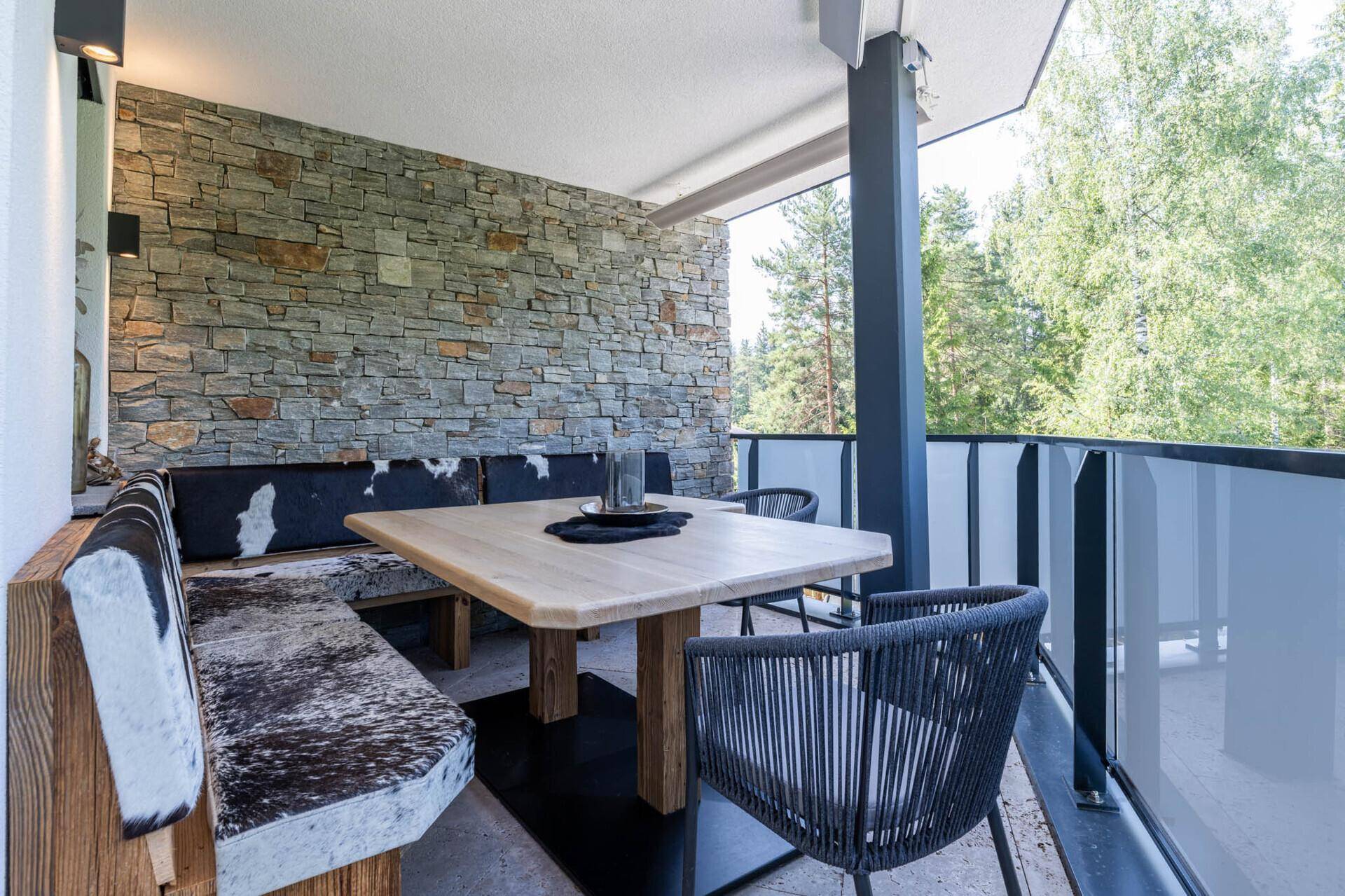 Geräumiger Balkon mit rustikalen Sitzgelegenheiten, Steinfassade und Blick ins Grüne.