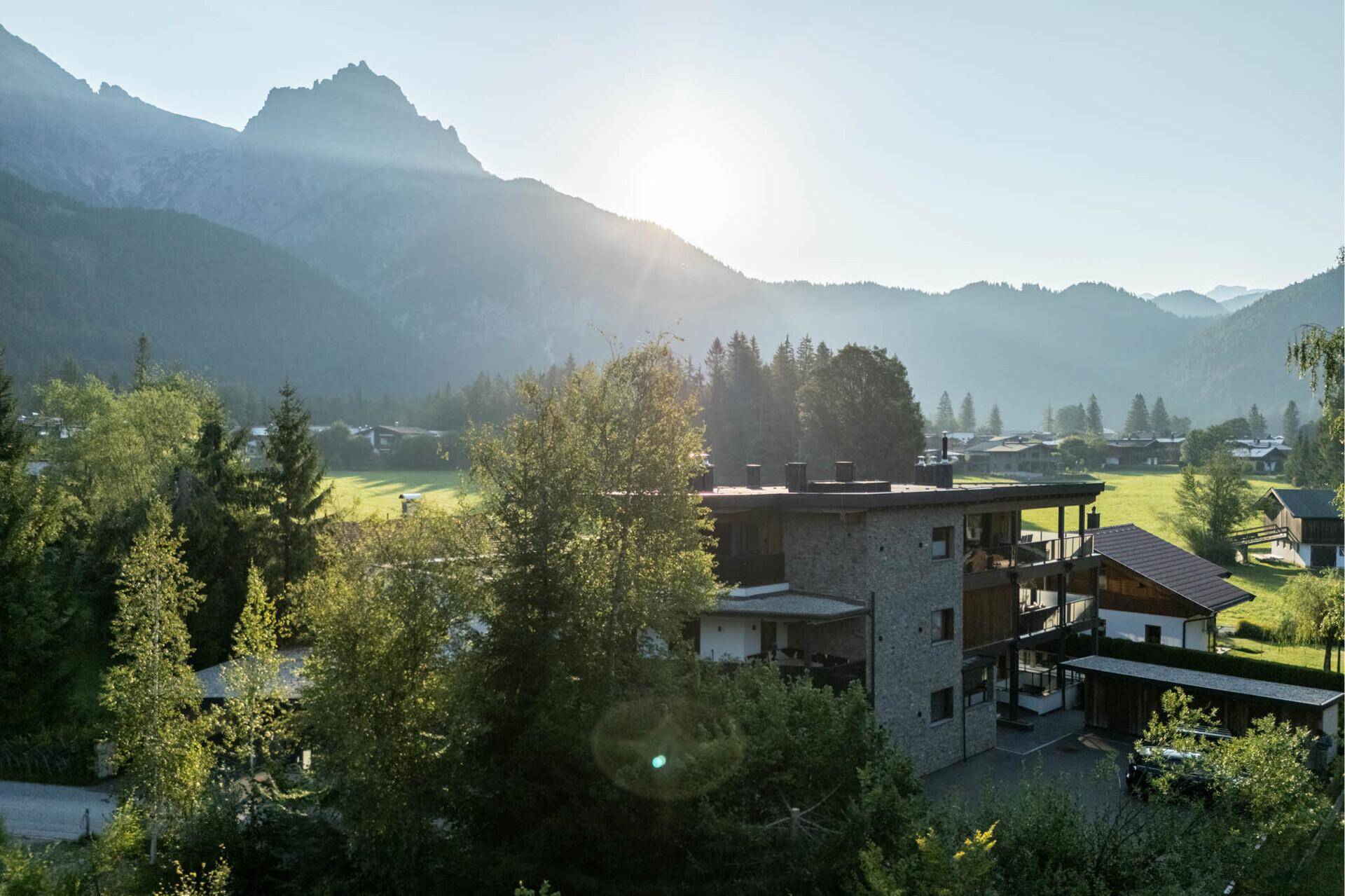 Modernes Gebäude in alpiner Landschaft mit Balkonen und sonnigem Bergblick.