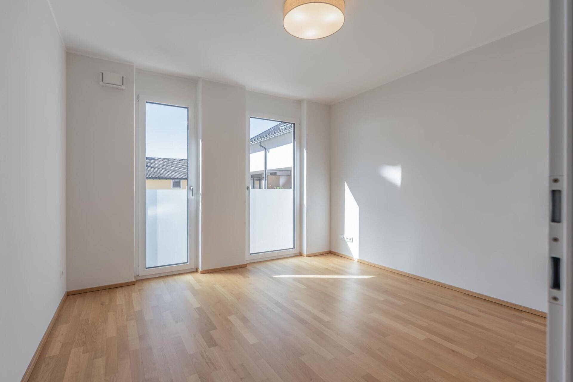 Lichtdurchflutetes Zimmer mit Holzboden und großen Fenstern, ideal als Schlaf- oder Arbeitszimmer.