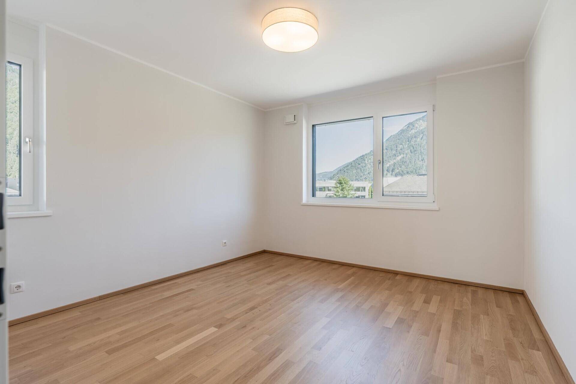 Helles Schlafzimmer mit Holzboden und Bergblick durch das Fenster.