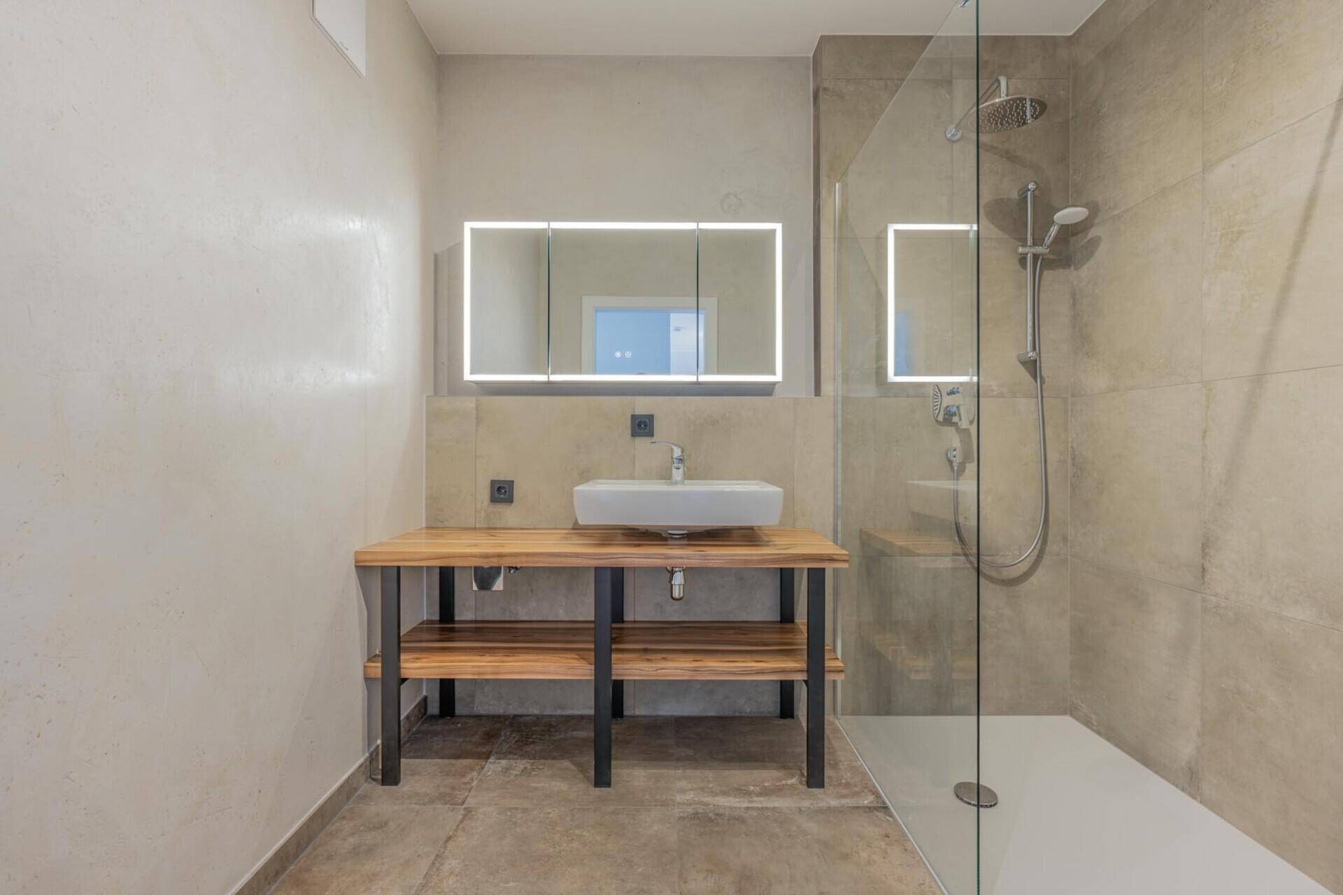 Modernes Badezimmer mit begehbarer Dusche, Holzwaschtisch und beleuchtetem Spiegelschrank.