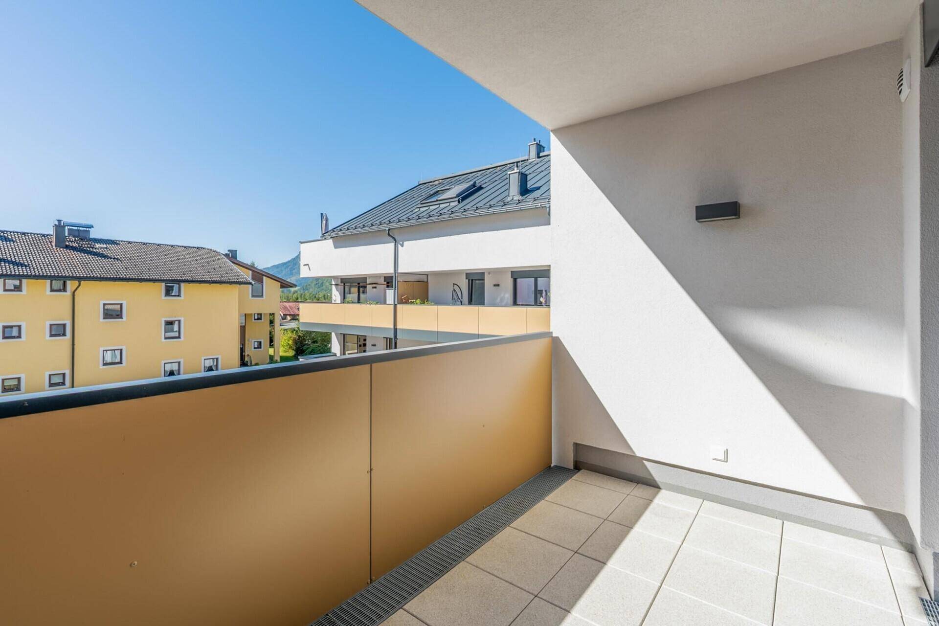 Heller Balkon mit Fliesenboden und Blick auf die umliegenden Gebäude und Berge.
