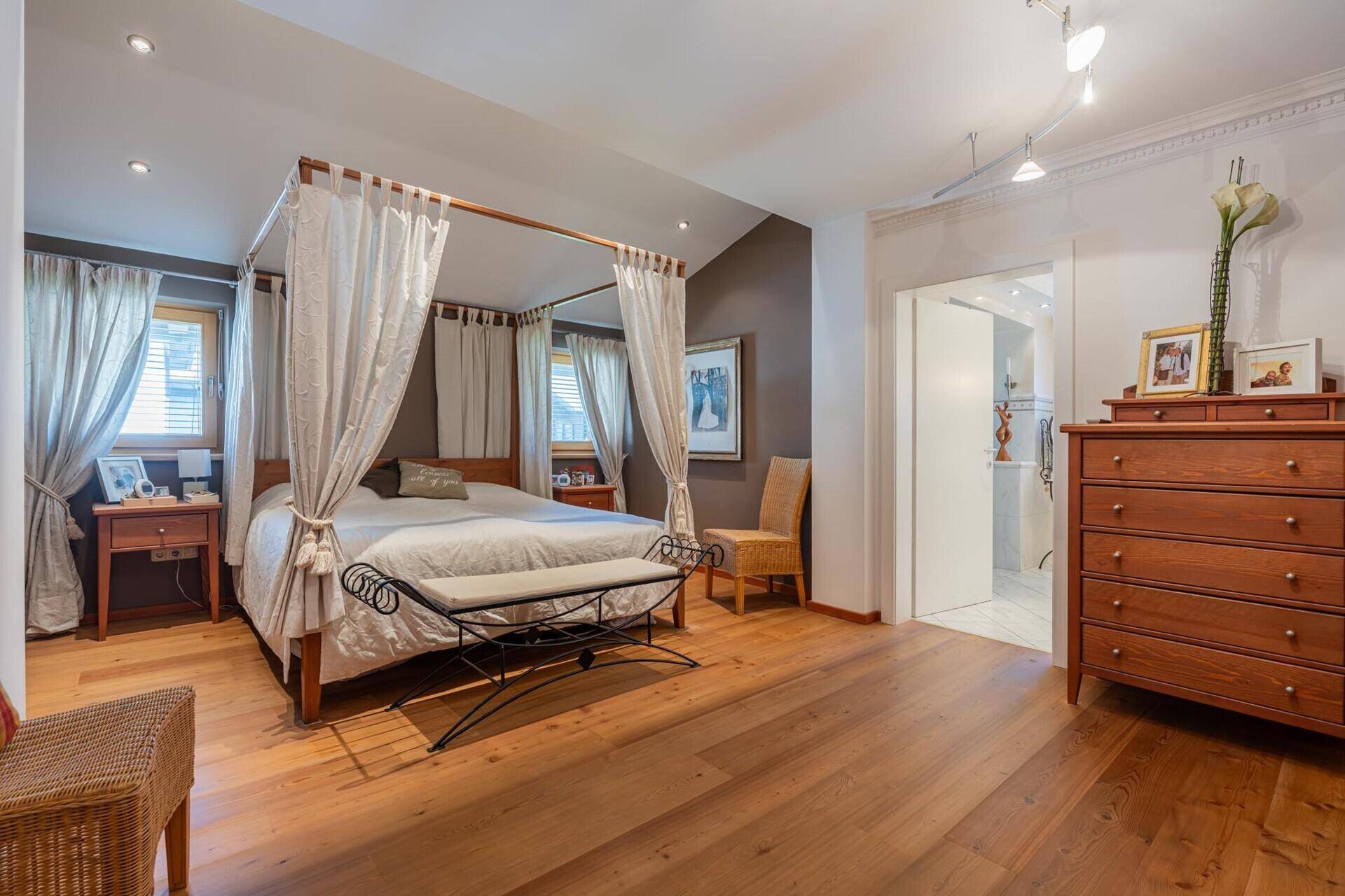 Geräumiges Schlafzimmer mit Himmelbett, Holzboden, hohen Decken und Zugang zum Bad.