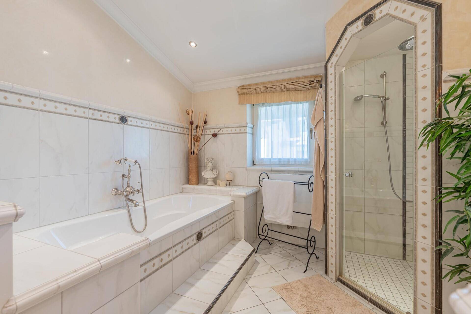 Helles Badezimmer mit Badewanne, Duschkabine, Fenster und beheiztem Handtuchhalter.