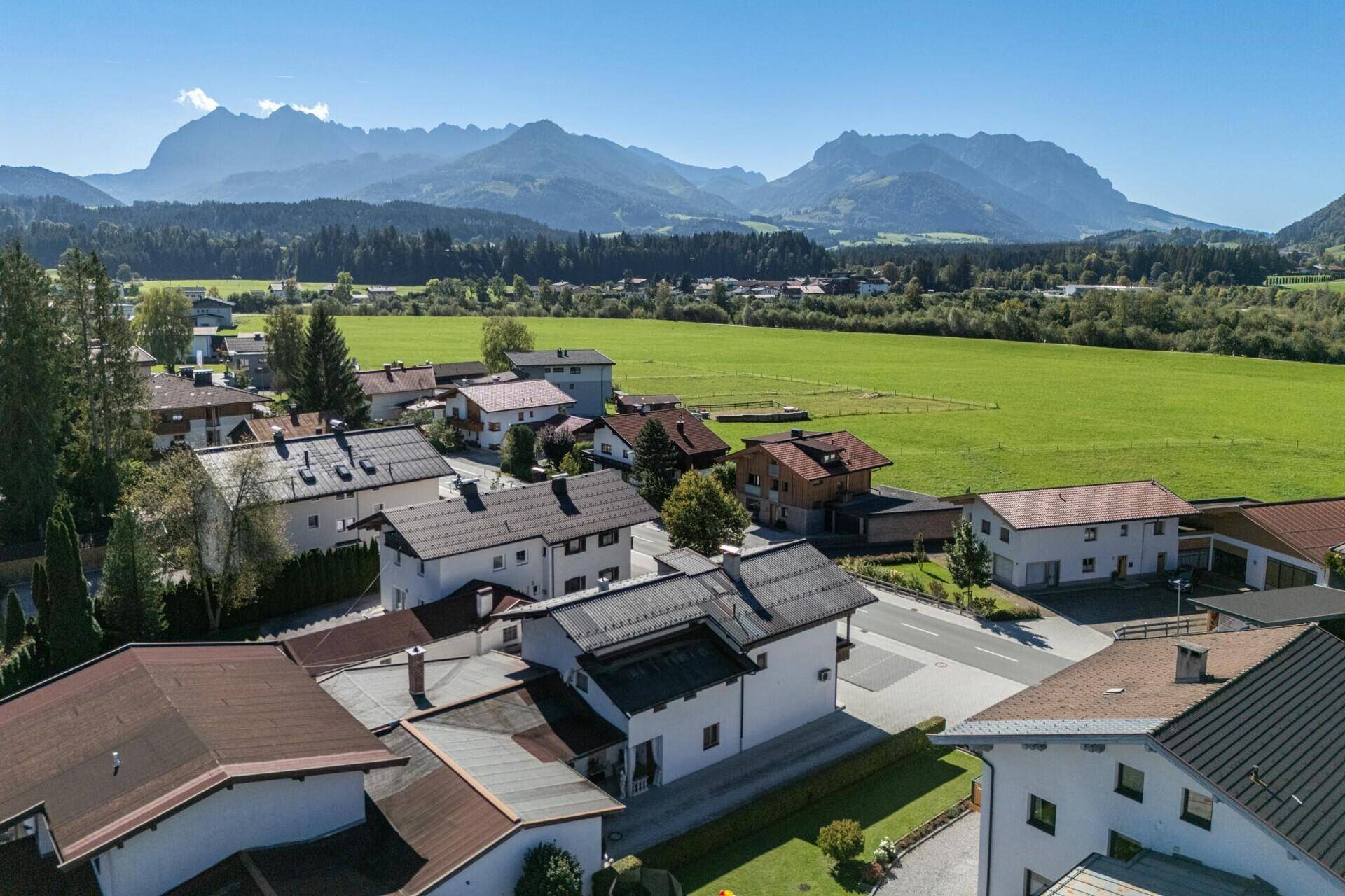 Luftaufnahme einer Wohnsiedlung mit grüner Landschaft und majestätischen Bergen im Hintergrund.