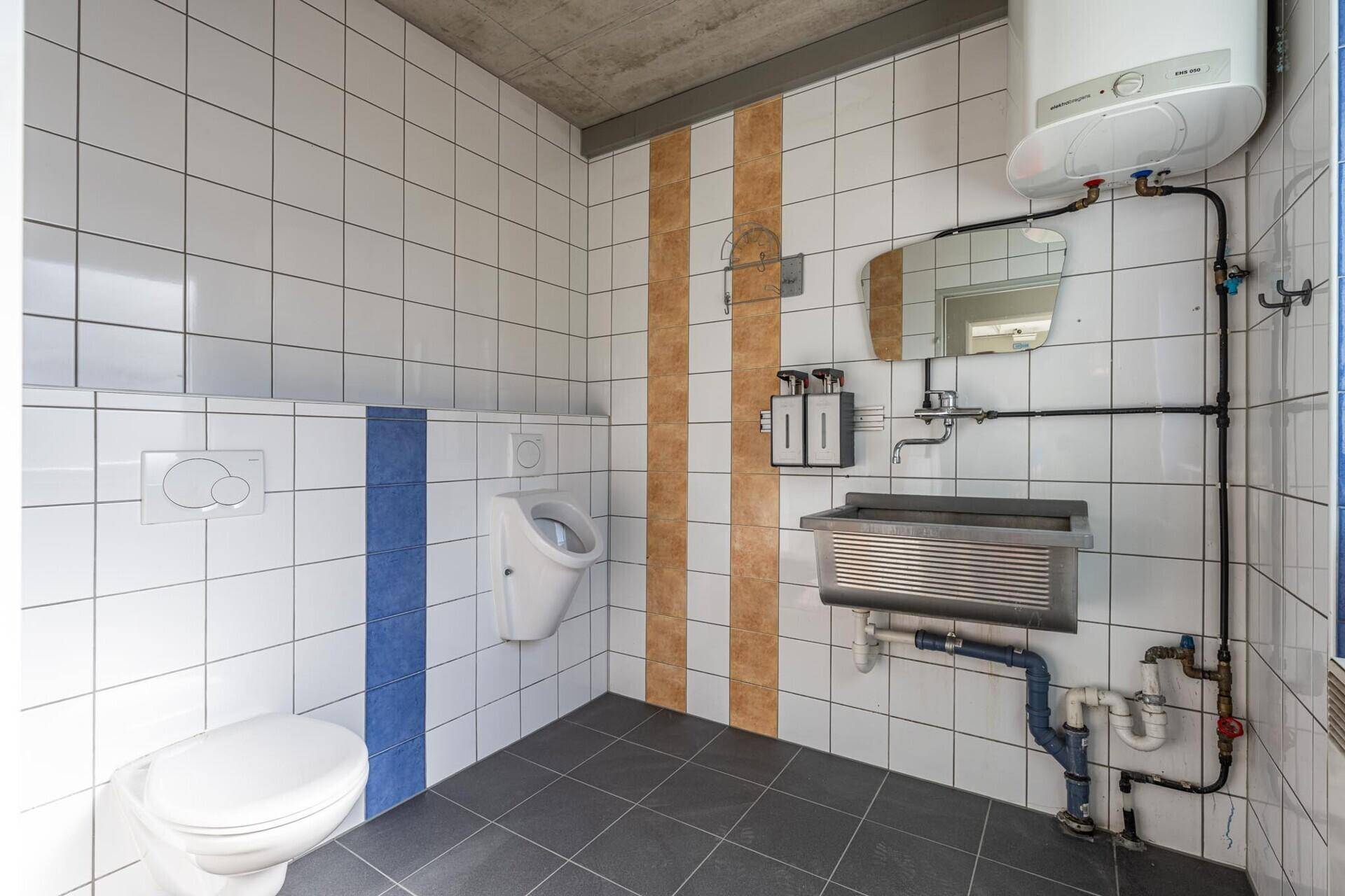 Funktionale Herrentoilette mit Urinal, Waschbecken, WC und Wandfliesen in Weiß und Blau.