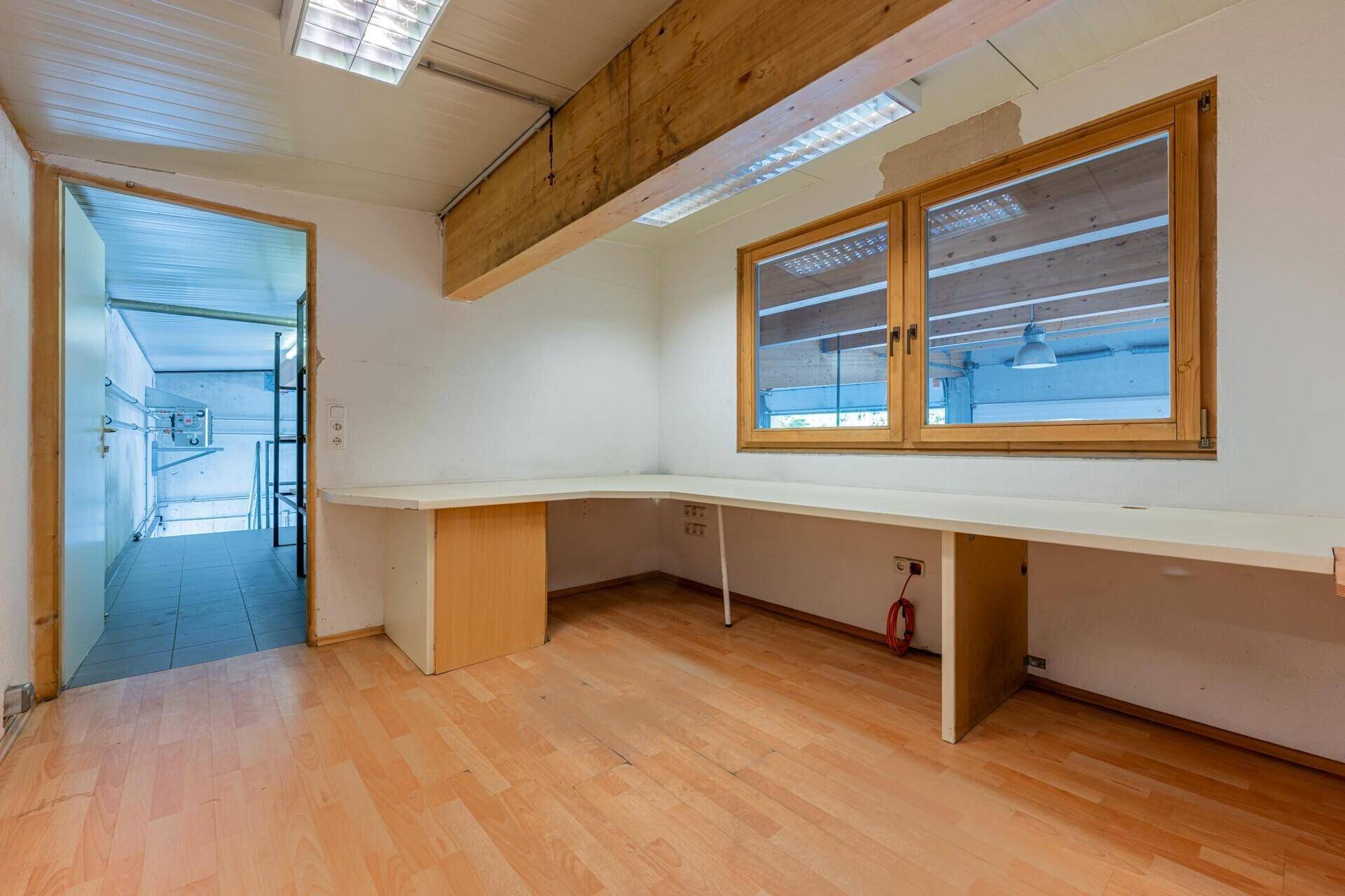 Helles Büro mit Holzboden, großen Fenstern und einem langen Schreibtisch unter sichtbaren Holzbalken.