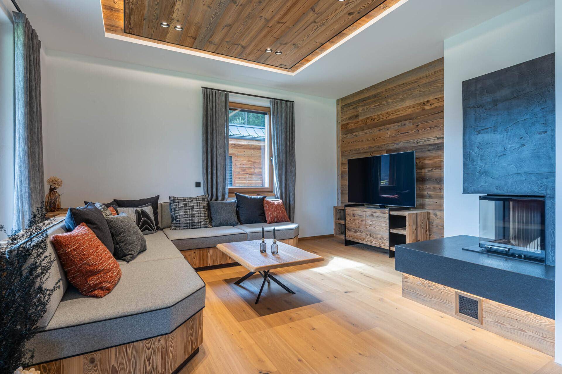 Gemütliches Wohnzimmer mit Holzboden, modernem Kamin und Holzwandverkleidung im alpinen Stil.