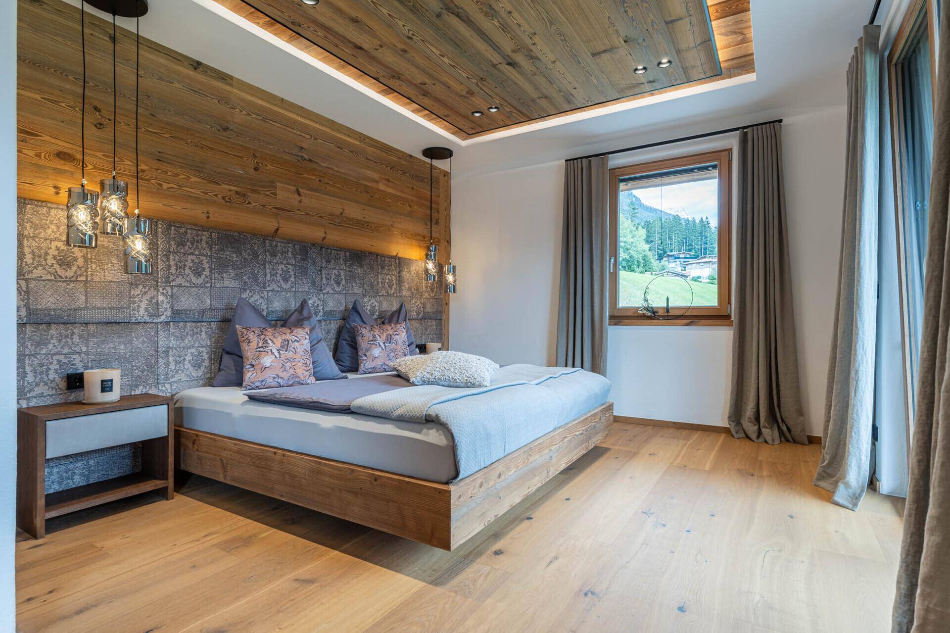 Helles Schlafzimmer mit Holzboden, Holzwand und einem Fenster mit Blick auf die grüne Landschaft.
