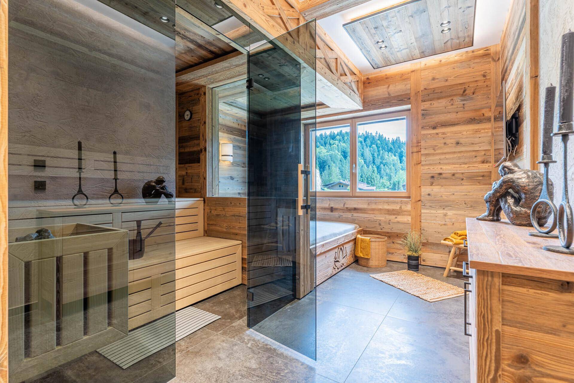 Moderner Wellnessbereich mit Sauna, Dusche und einem Fenster mit Blick auf die umliegende Berglandschaft.