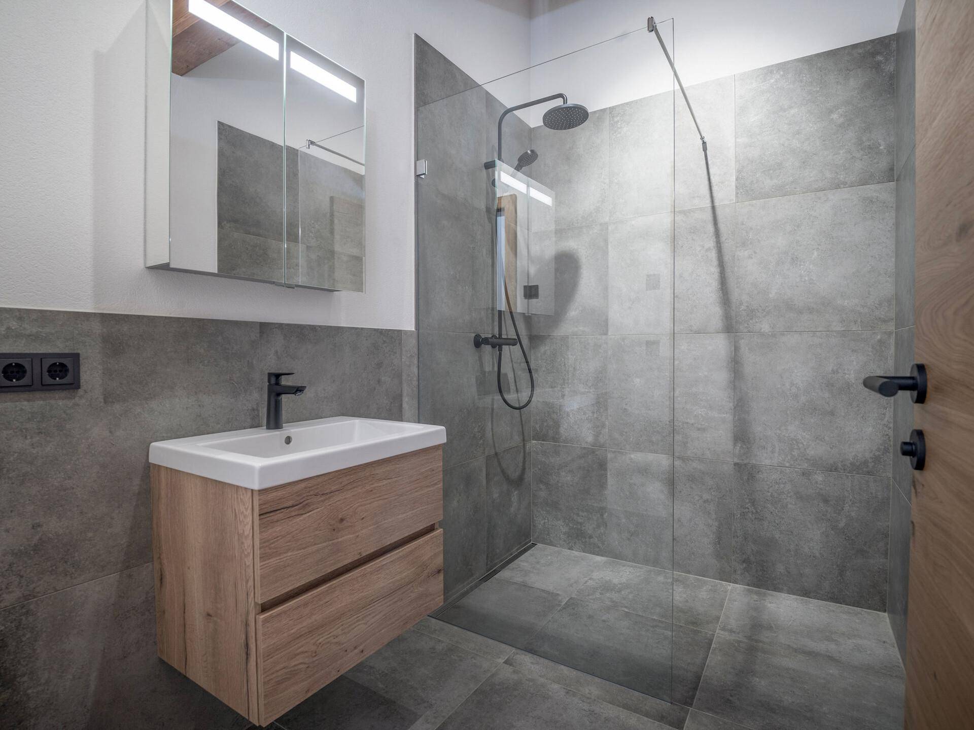 Modernes Badezimmer mit Einzelwaschbecken, Spiegelschrank und großer begehbarer Dusche.