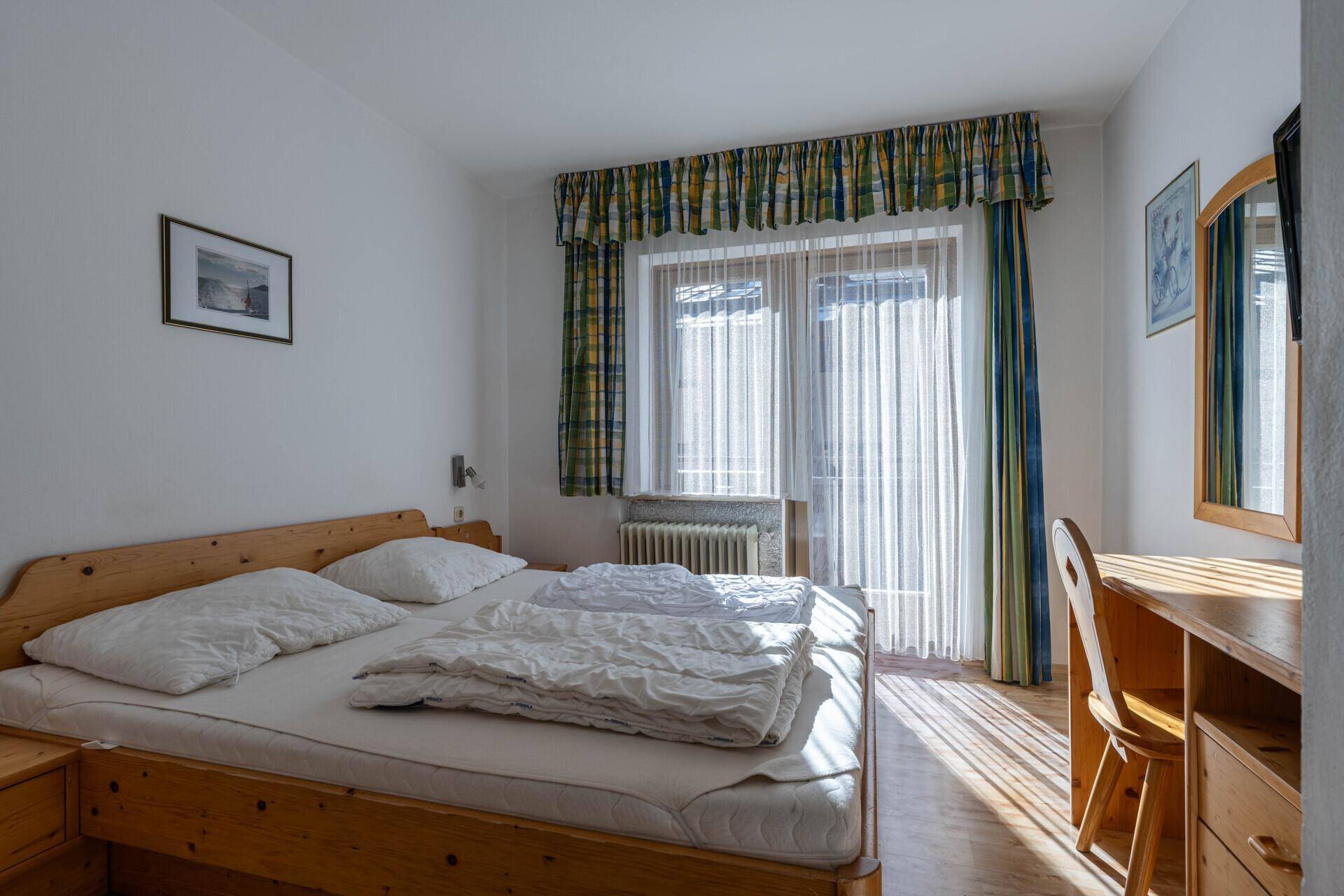 Helles Schlafzimmer mit zwei Einzelbetten, Holzboden und Zugang zu einem Balkon.