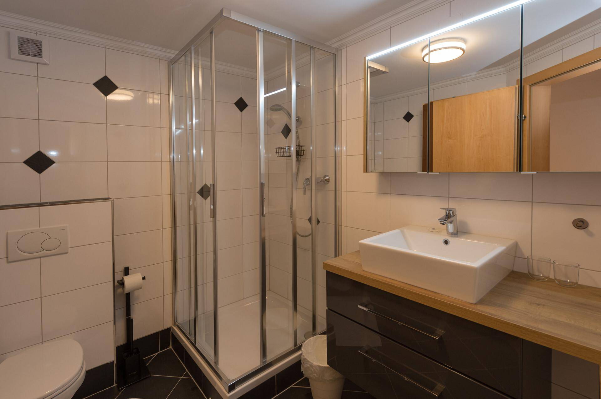 Modern gefliestes Badezimmer mit Duschkabine, Waschtisch und integriertem Spiegelschrank.