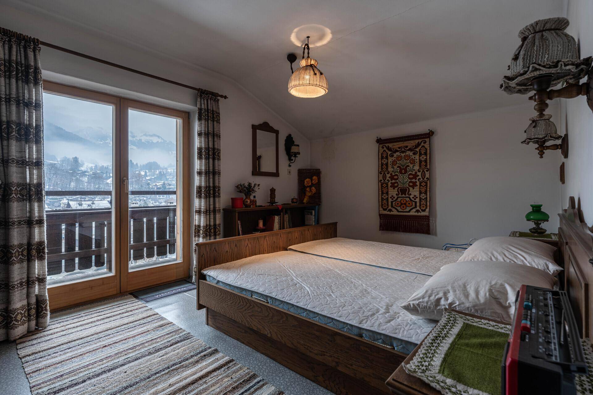 Gemütliches Schlafzimmer mit traditioneller Einrichtung, Balkonzugang und Bergblick auf die verschneite Landschaft.