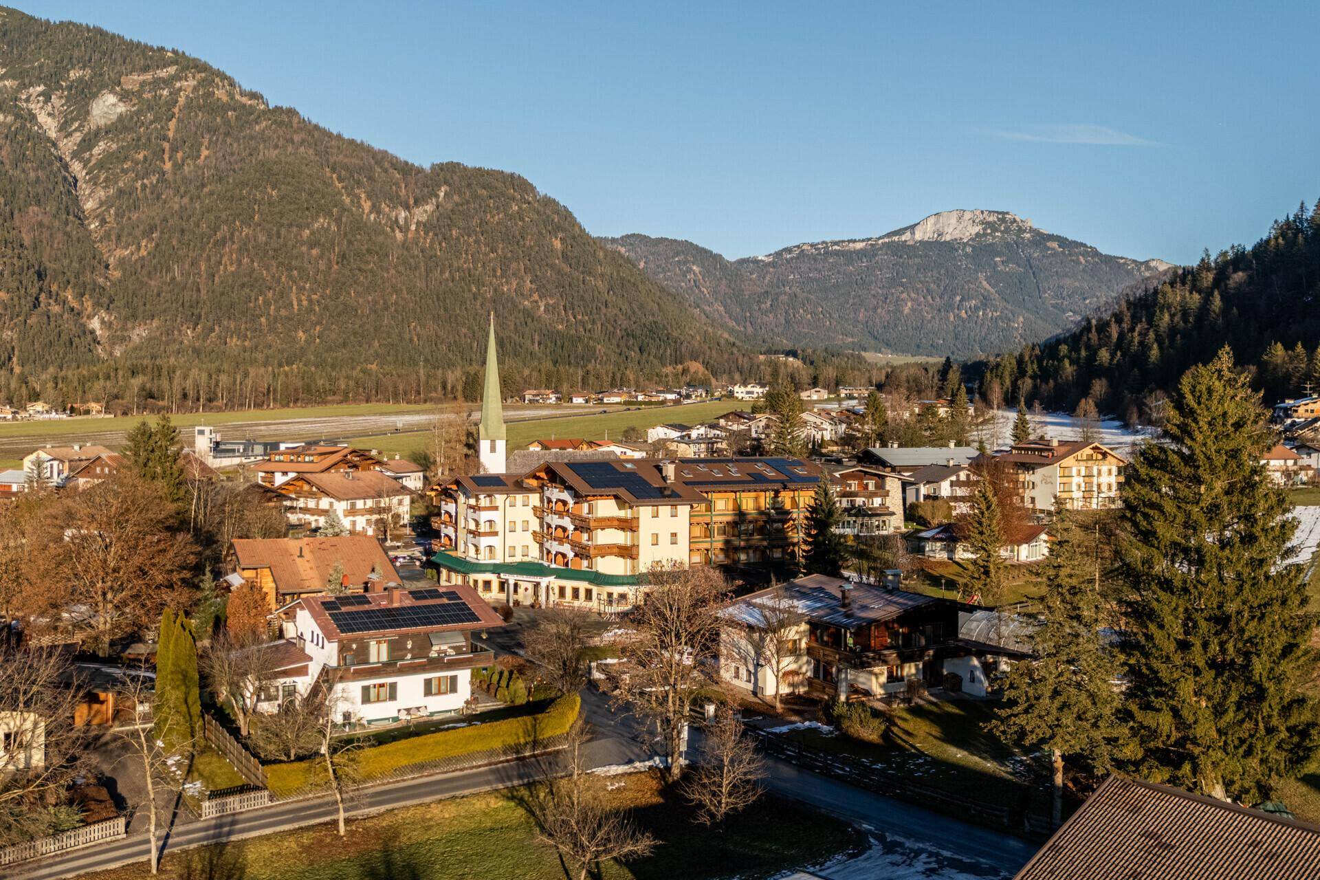 Panoramablick auf ein malerisches Dorf in einem Tal, umgeben von schneebedeckten Bergen und Wäldern.