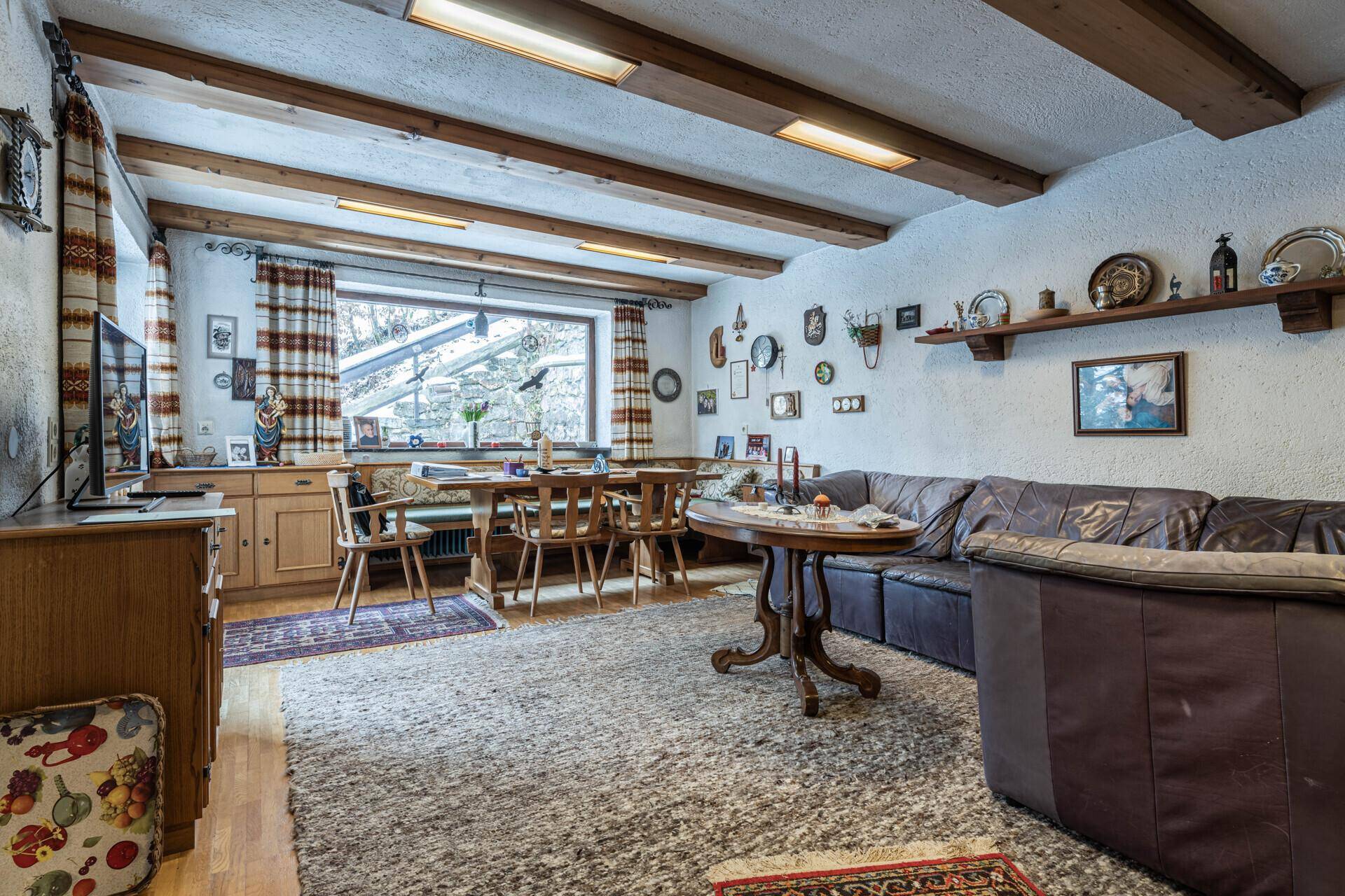 Rustikaler Wohn-Essbereich mit Holzbalkendecke, großer Eckbank und gemütlichem Ledersofa.
