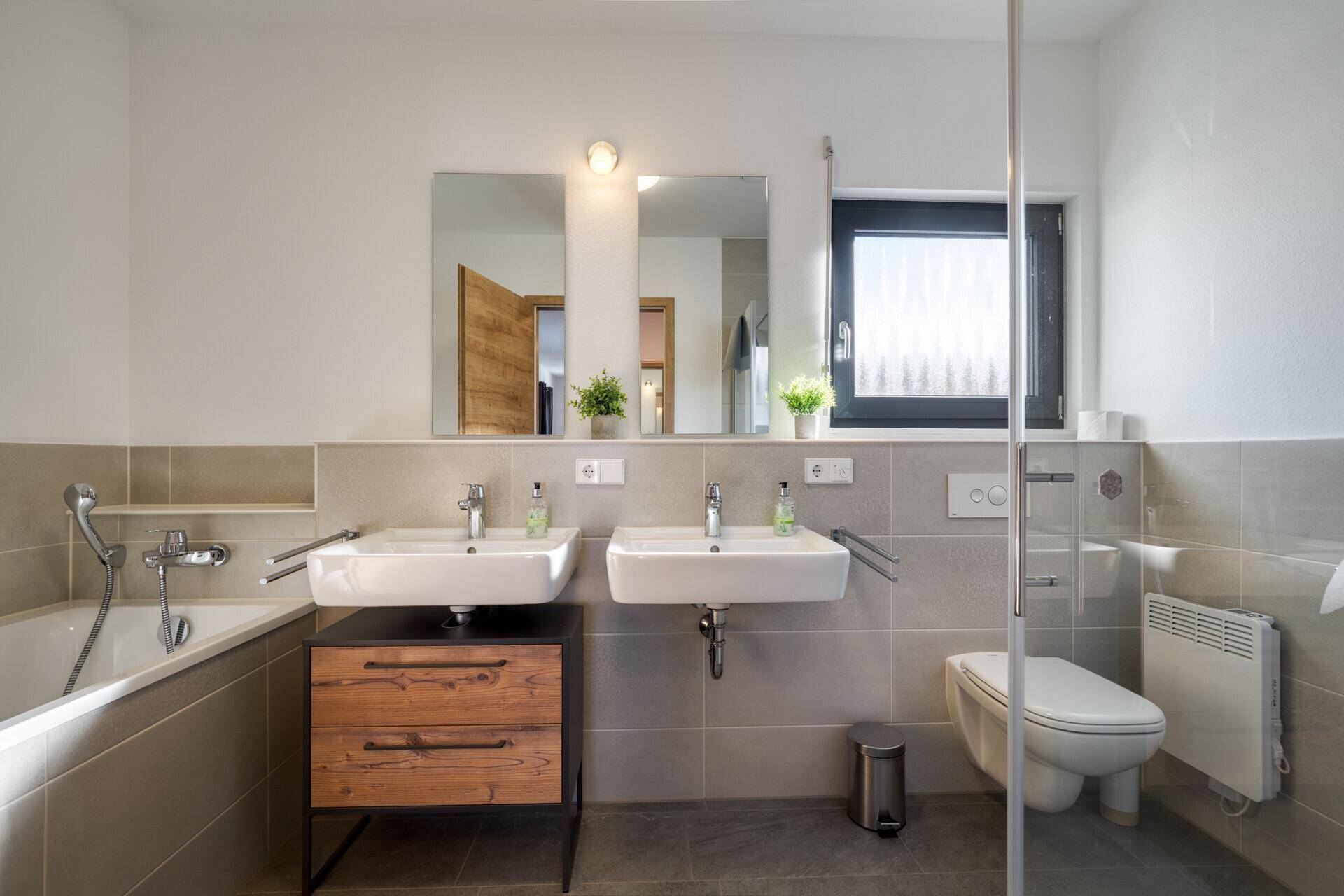 Helles Badezimmer mit Badewanne, Doppelwaschbecken und modernen Fliesen.