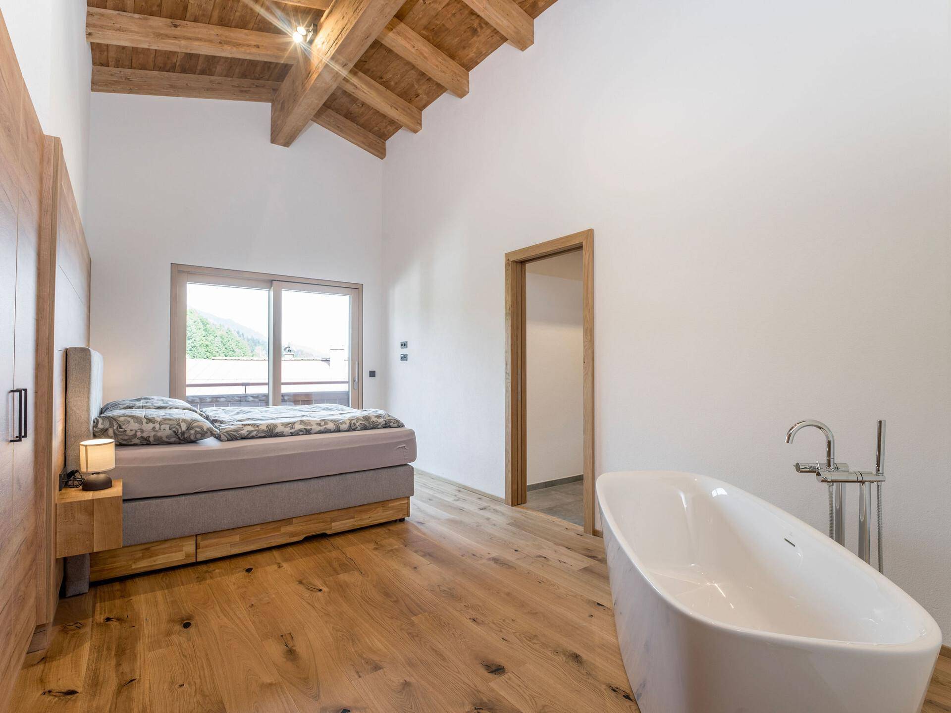Schlafzimmer mit freistehender Badewanne, Holzboden und Zugang zu einem Außenbereich.