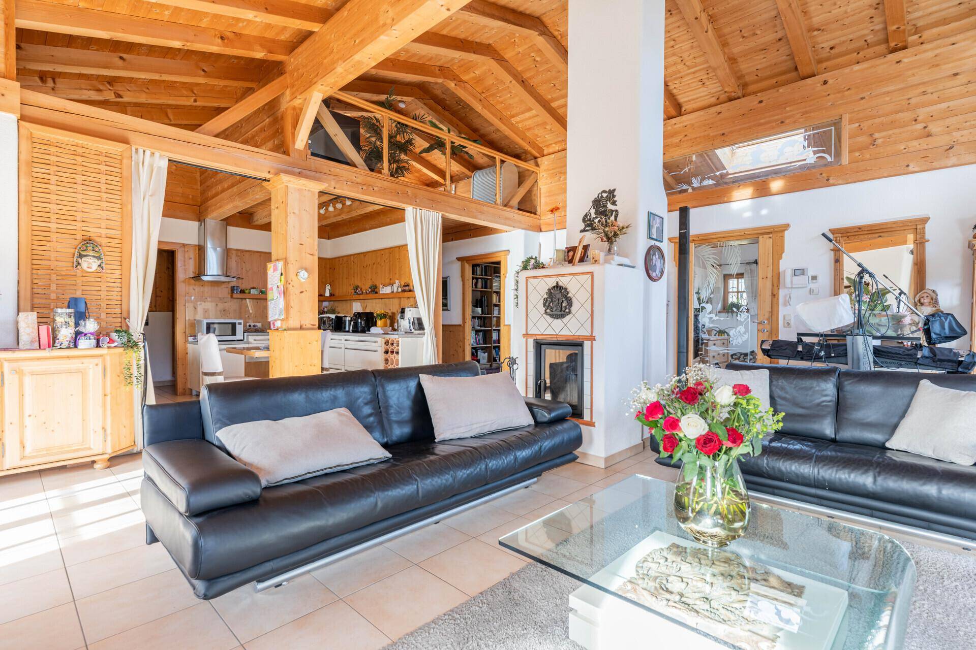 Heller Wohnbereich mit Ledersofas, Holzbalken und offener Küche im Hintergrund.
