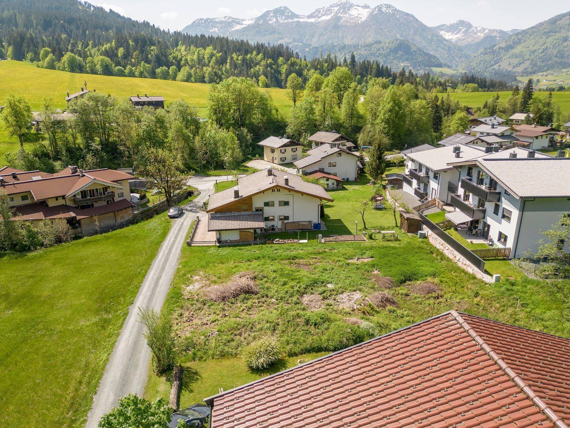 Luftaufnahme einer Wohnsiedlung eingebettet in eine weite grüne Landschaft mit Bergen.