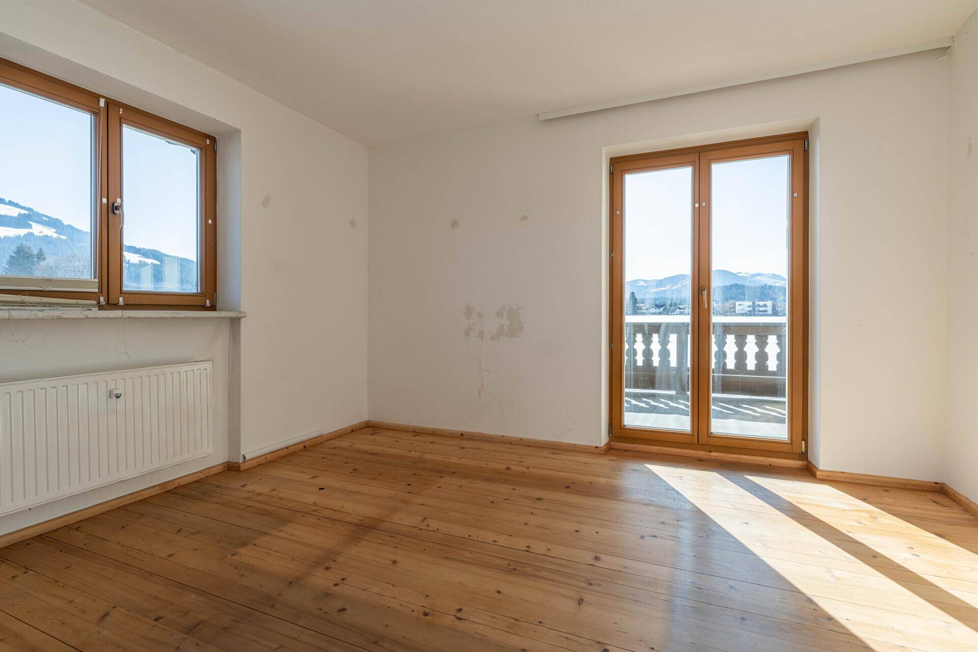 Helles Schlafzimmer mit Holzdielenboden und Zugang zu einem traditionellen Balkon mit Bergblick.