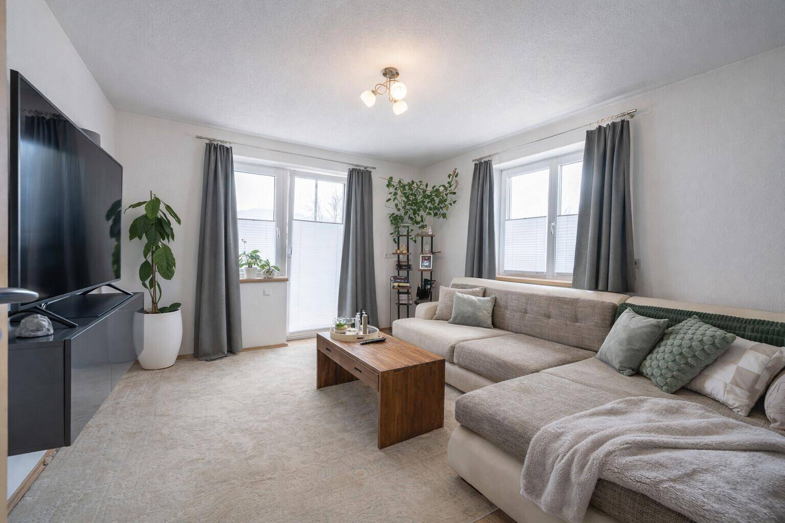 Helles Wohnzimmer mit großem Ecksofa, Teppichboden und viel Tageslicht durch die Fenster.