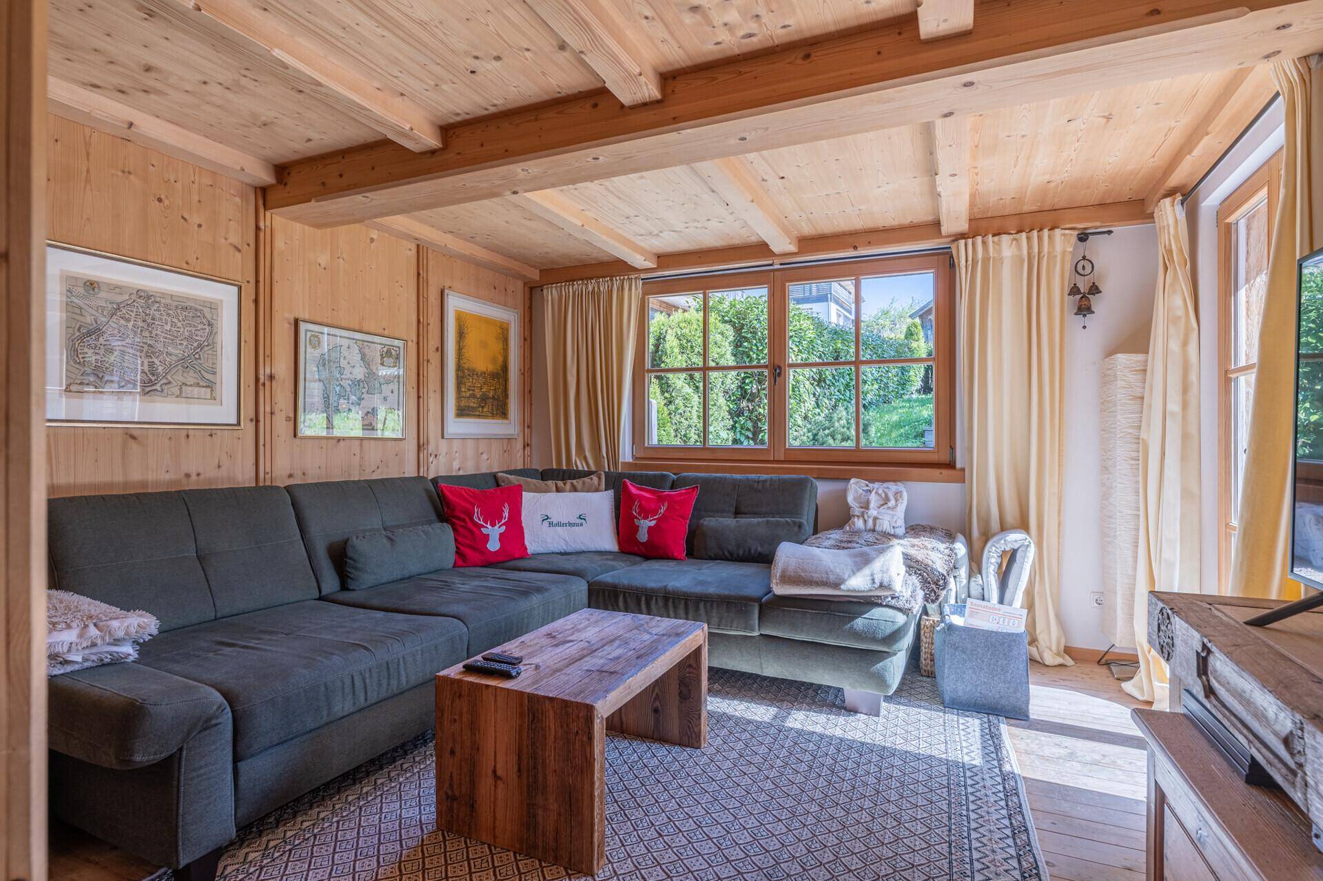 Helles Wohnzimmer mit großer Eckcouch, Holztisch und Blick ins Grüne durch das Fenster.