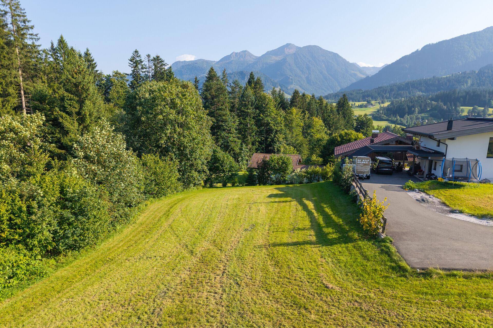 Große, gepflegte Rasenfläche mit Waldrand und beeindruckendem Bergblick in der Ferne.