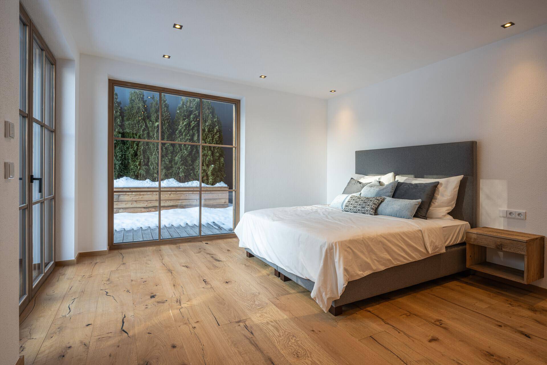 Helles Schlafzimmer mit großem Fenster, Holzboden und direktem Zugang zur Terrasse oder Balkon.