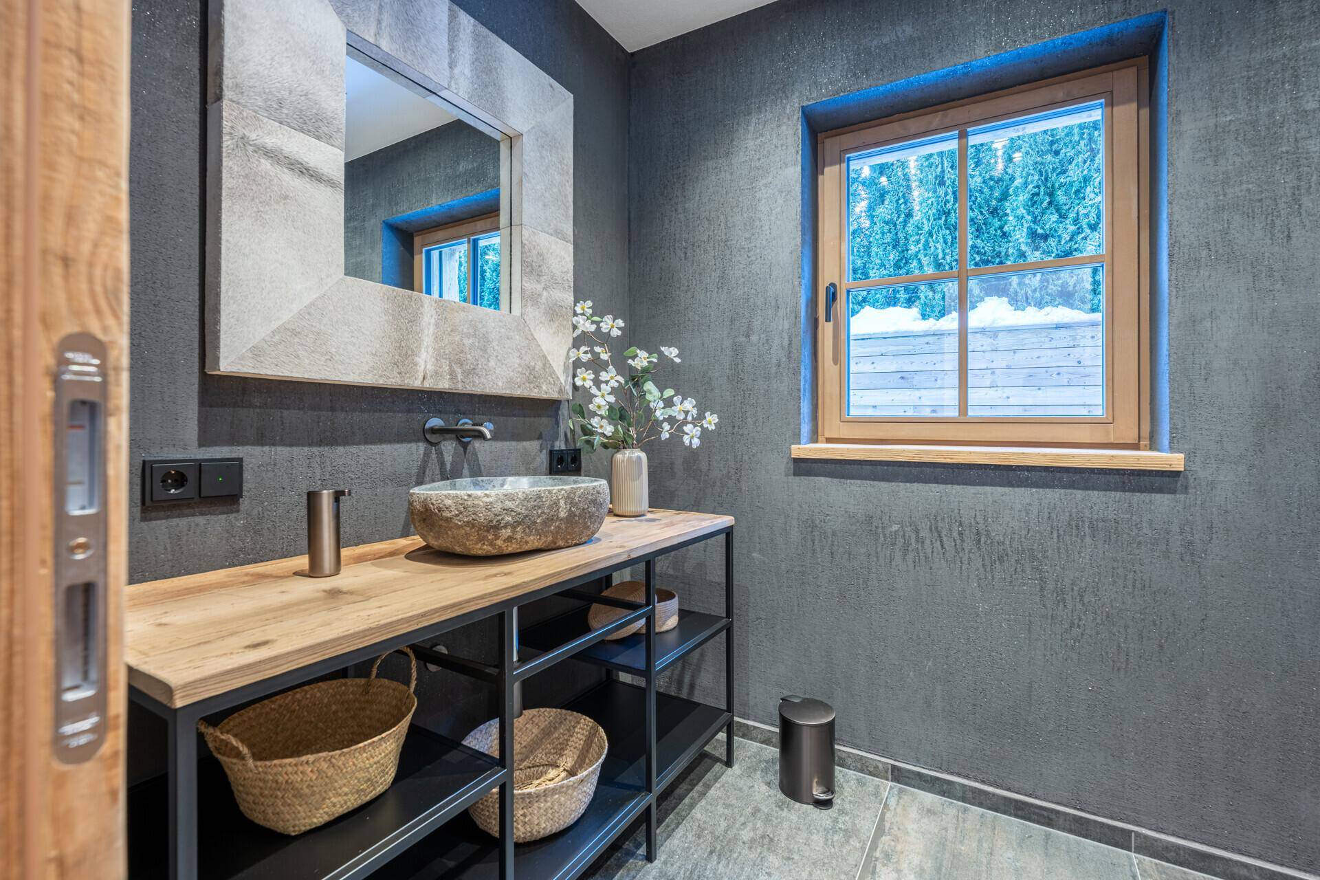 Stilvolles Badezimmer mit Steinwaschbecken, Holzkonsole und Fenster für natürliches Licht.