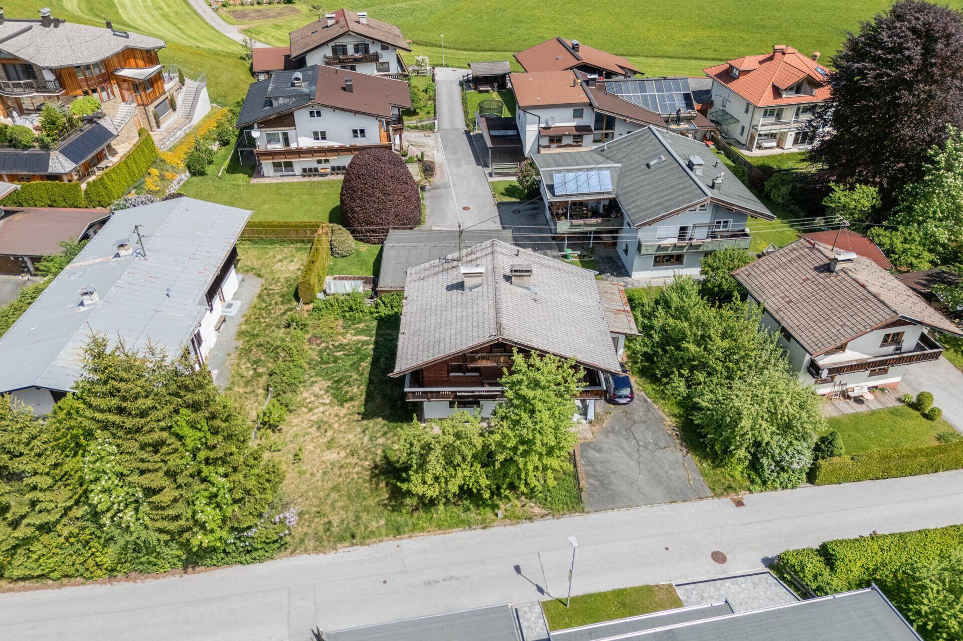 Luftaufnahme eines Hauses mit großem Grundstück und angrenzenden Wohnhäusern in alpiner Landschaft.
