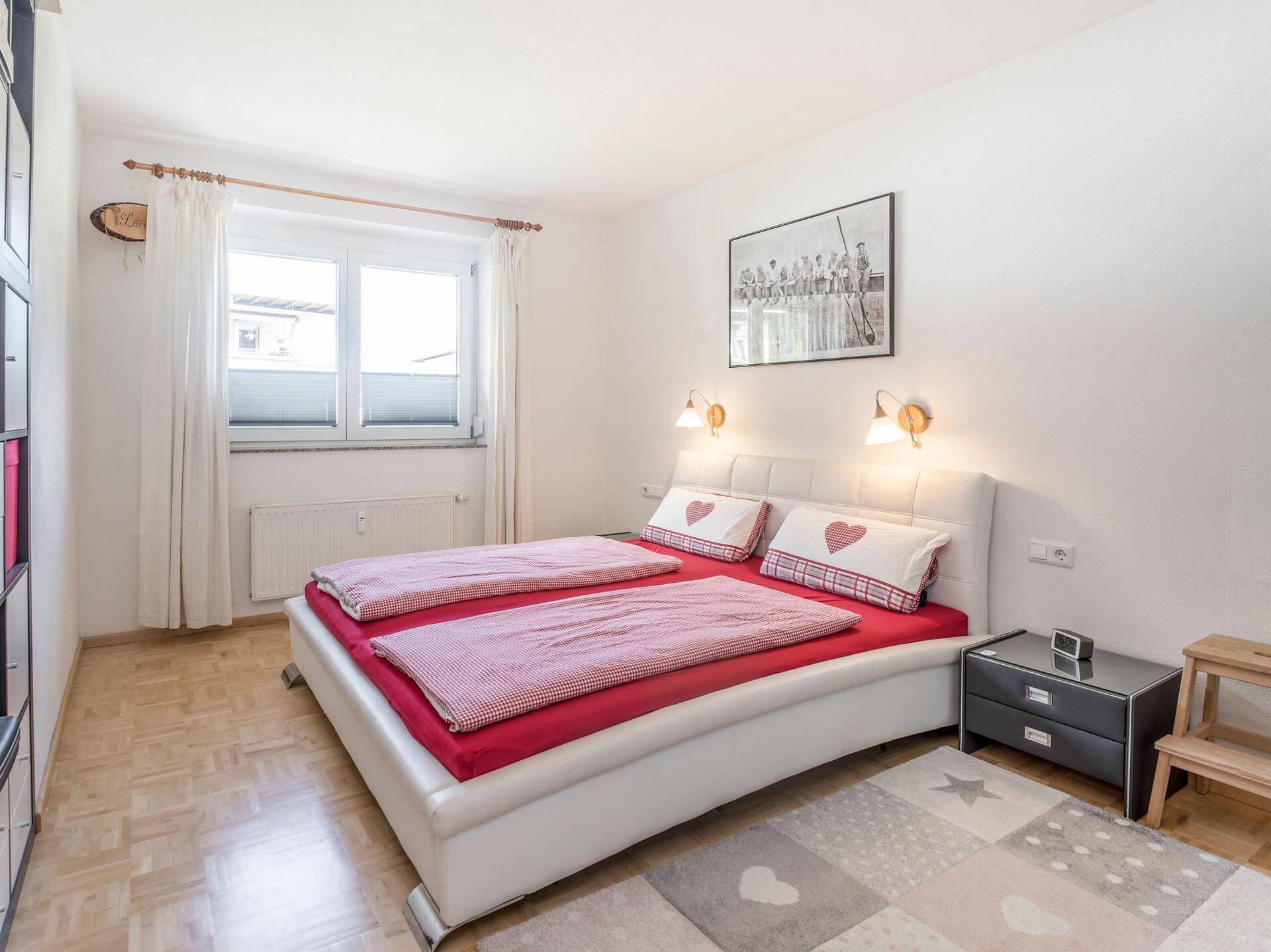 Gemütliches Schlafzimmer mit Doppelbett, Holzparkettboden und Fenster mit Plissee-Jalousien.