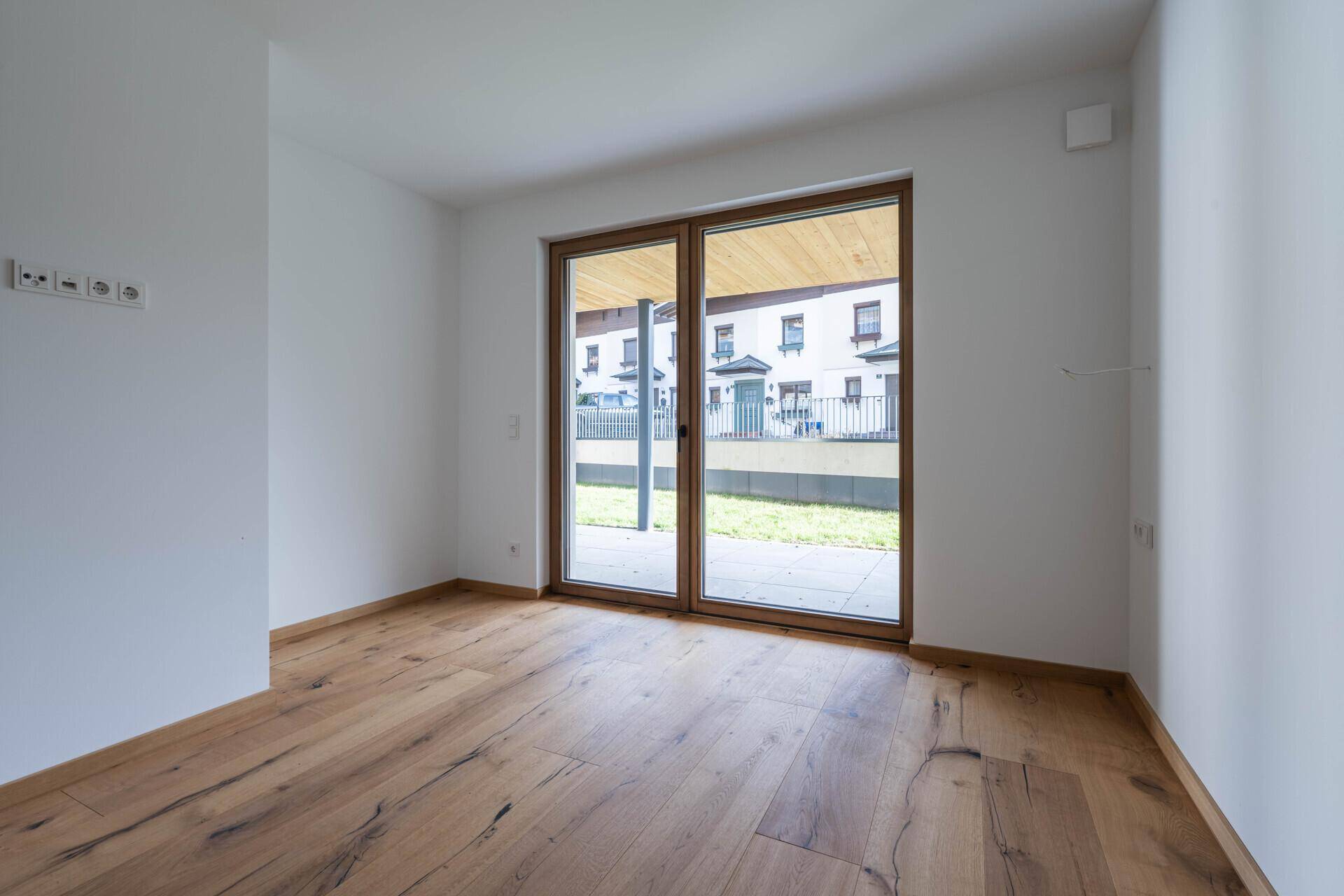 Lichtdurchfluteter Raum mit Holzboden und großer Terrassentür zum Außenbereich.