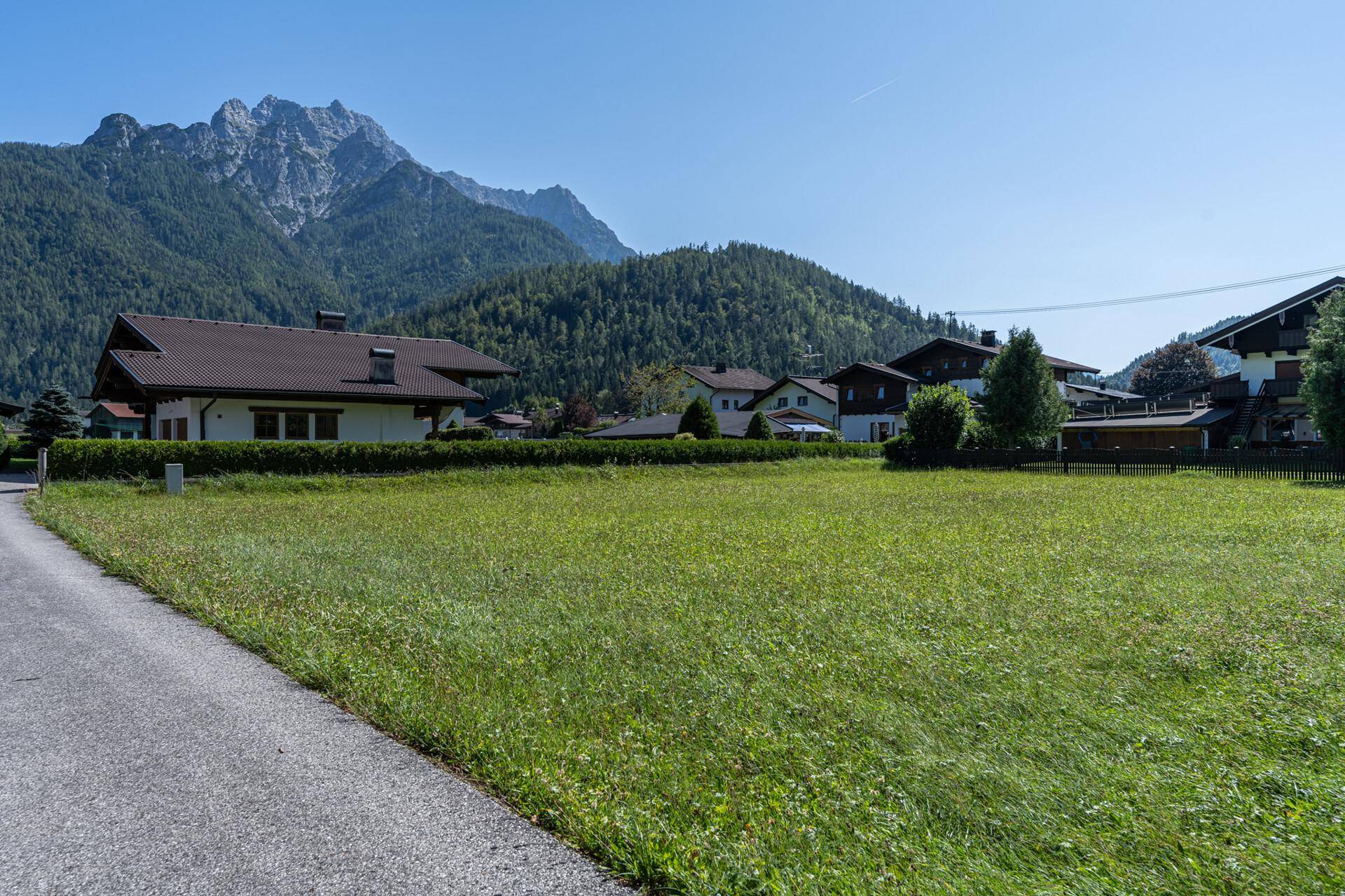 Blick über das grüne Grundstück auf die umliegende Berglandschaft unter blauem Himmel.