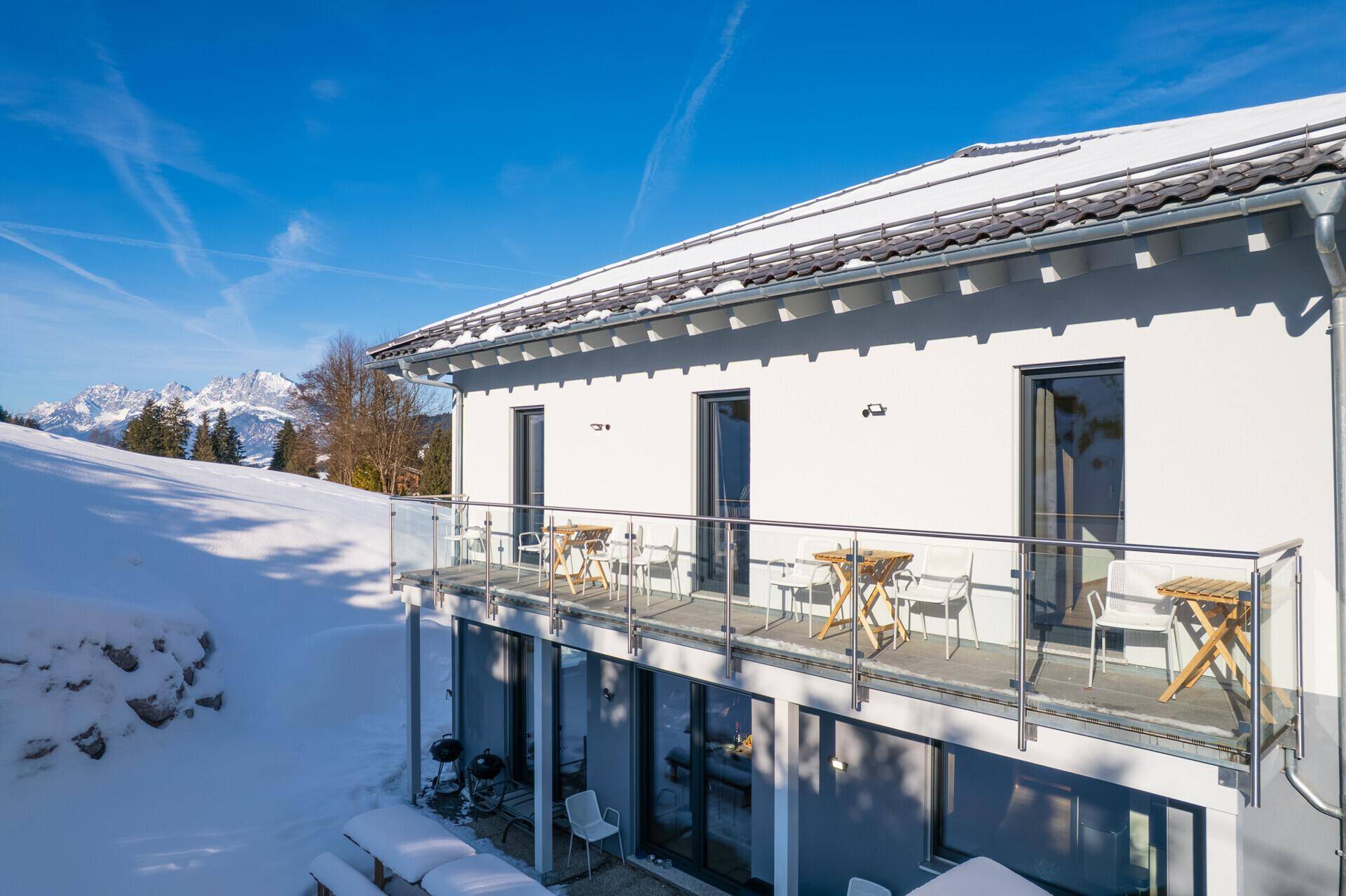 Großer Balkon mit Glasgeländer, Sitzgelegenheiten und weitem Blick auf die Berge.