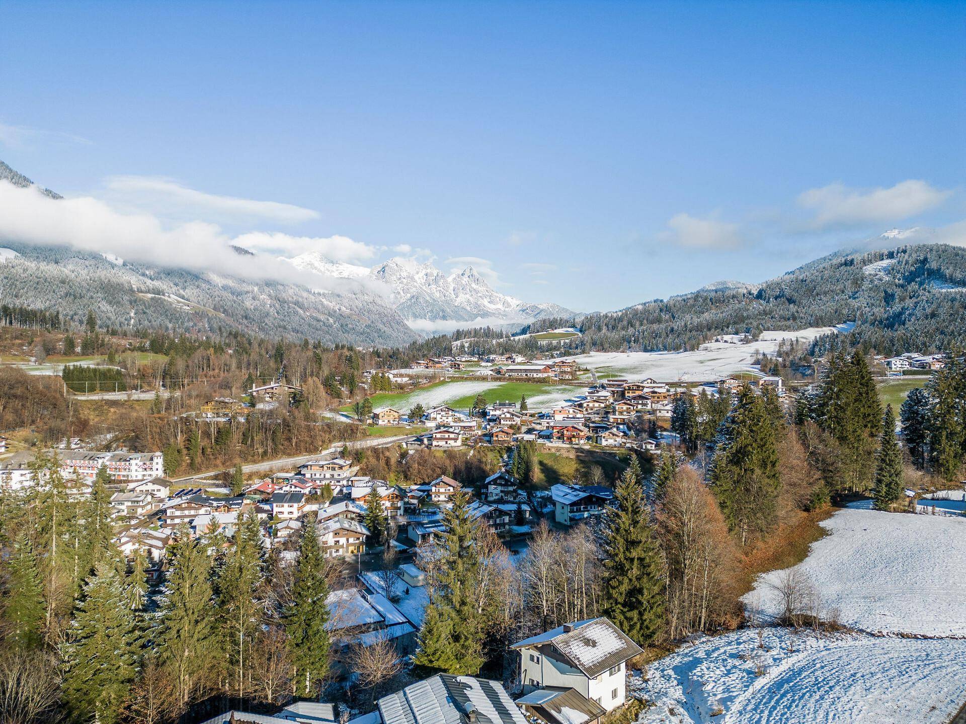 Weitläufige Ansicht eines malerischen Dorfes im Tal, umgeben von verschneiten Bergen.