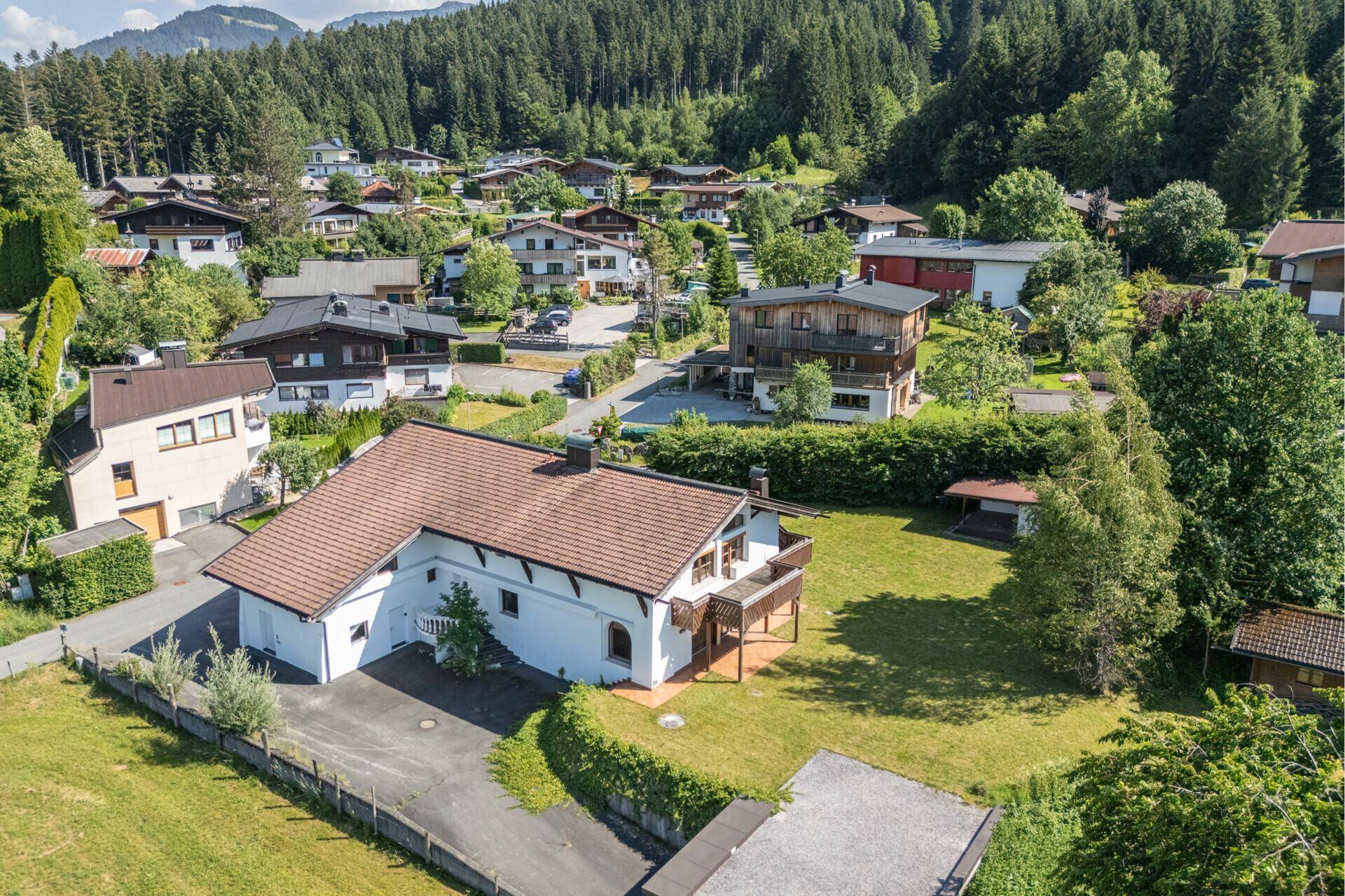 Luftaufnahme eines Wohnhauses mit Garten und umliegender Bebauung, eingebettet in eine grüne Landschaft.