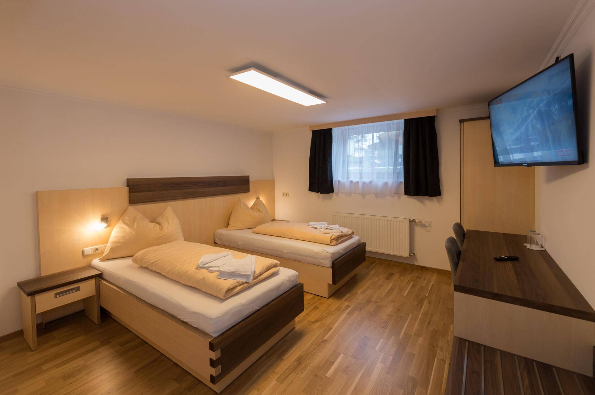 Gemütliches Schlafzimmer mit zwei Einzelbetten, Holzboden und einem an der Wand montierten Fernseher.