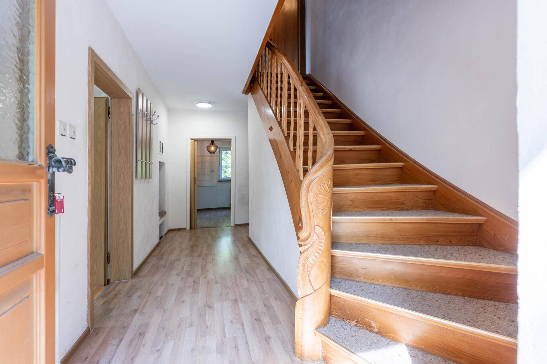 Heller Flur mit einer kunstvoll geschnitzten Holztreppe und Holzböden.