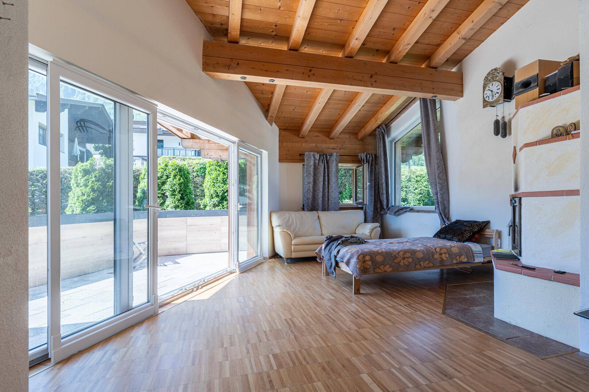 Helles Wohnzimmer mit Holzbalkendecke, Parkettboden, großzügigen Glasfronten und Kachelofen.