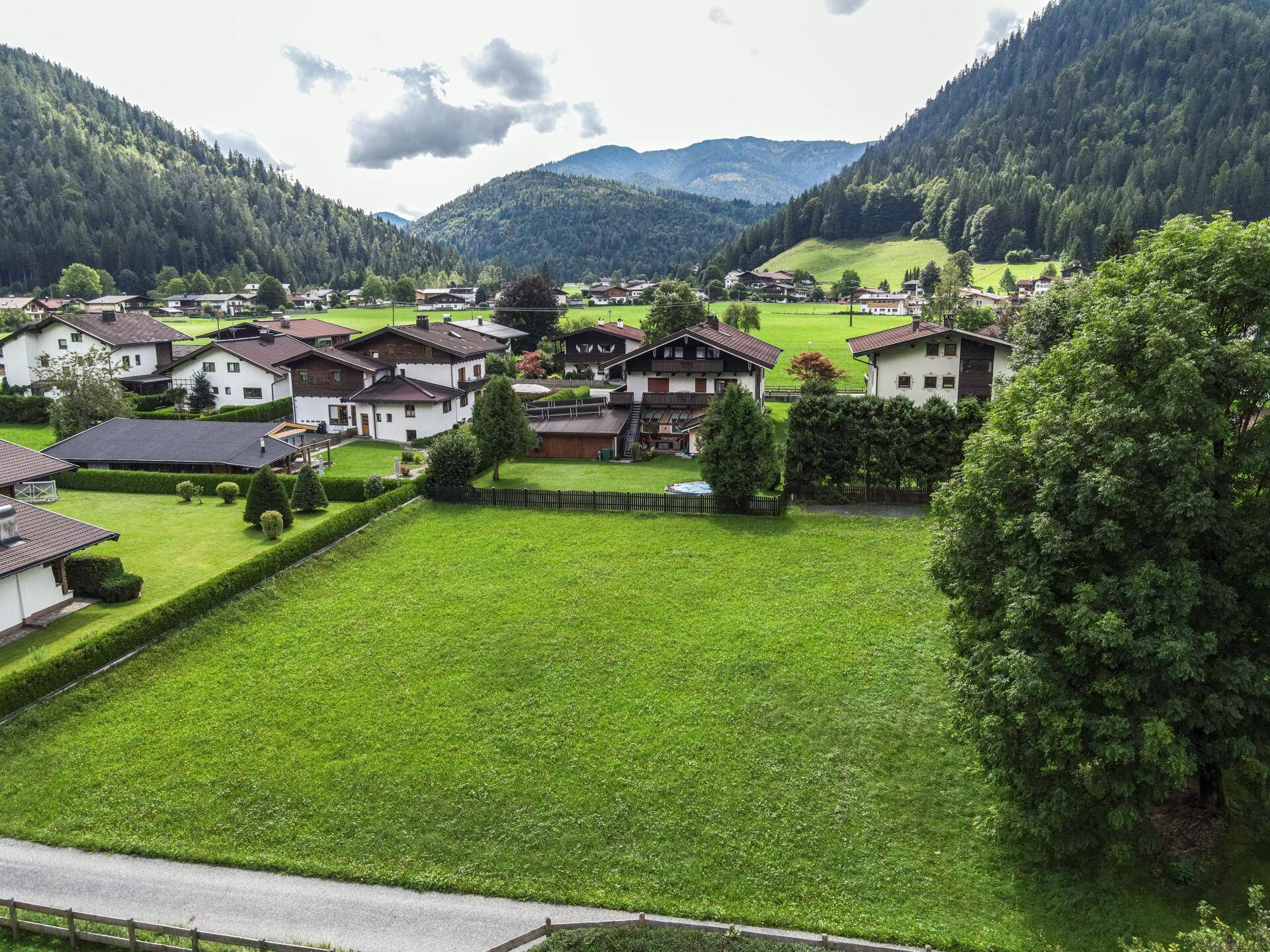 Weitläufige Ansicht eines grünen Grundstücks mit Dorfbebauung und majestätischen Bergen im Hintergrund.